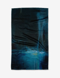 The Grotto tea towel by Jennifer Janesko features abstract blue and black patterns with lighter blue and white brushstrokes, accented by vertical streaks. Crafted from recycled materials, its a stylish, eco-friendly choice for your home.