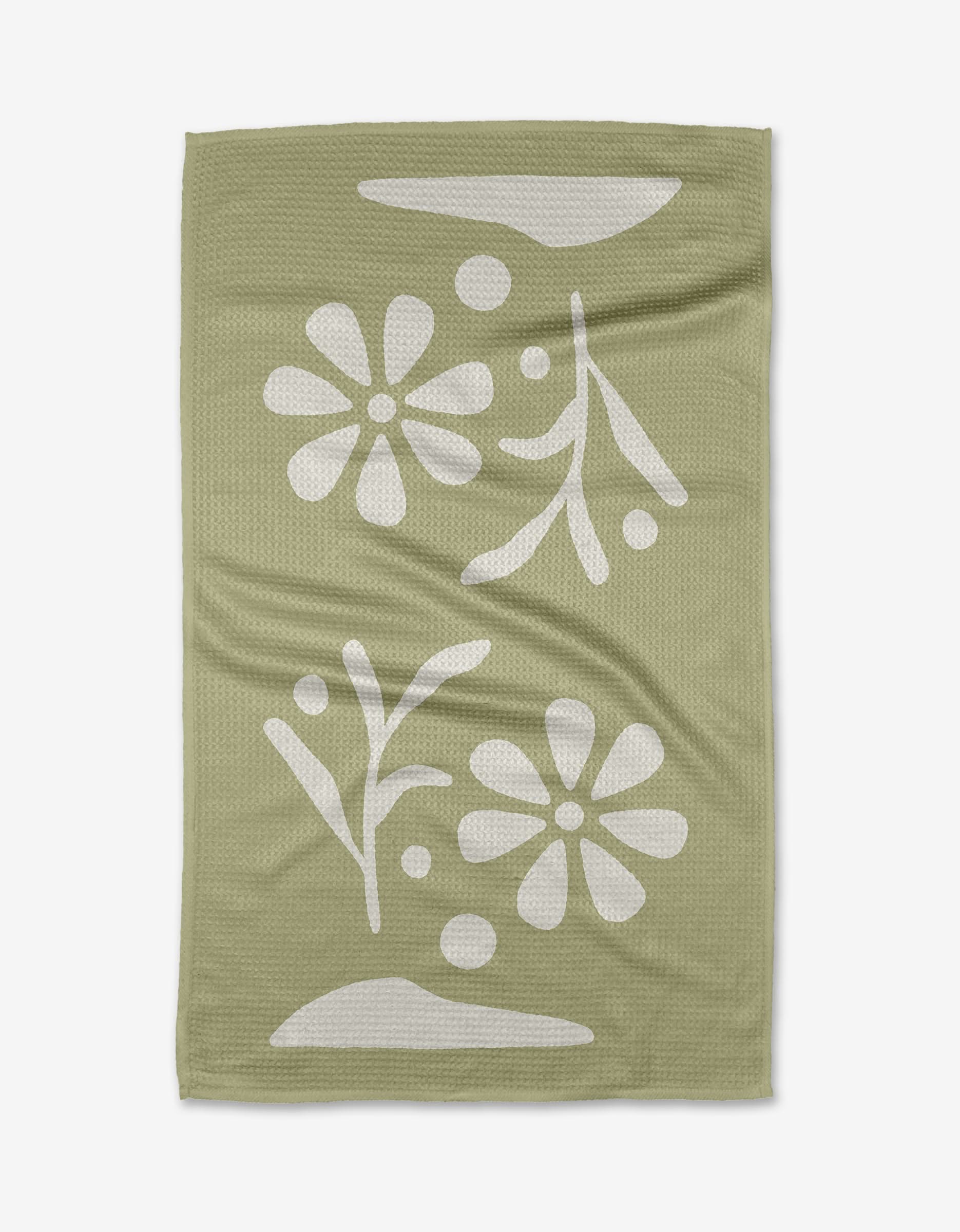 The Honey Dew tea towel by Graphics and Grain features a sage green, textured surface with a white floral and leaf pattern, abstract shapes, and dots. Made from quick-drying recycled materials.