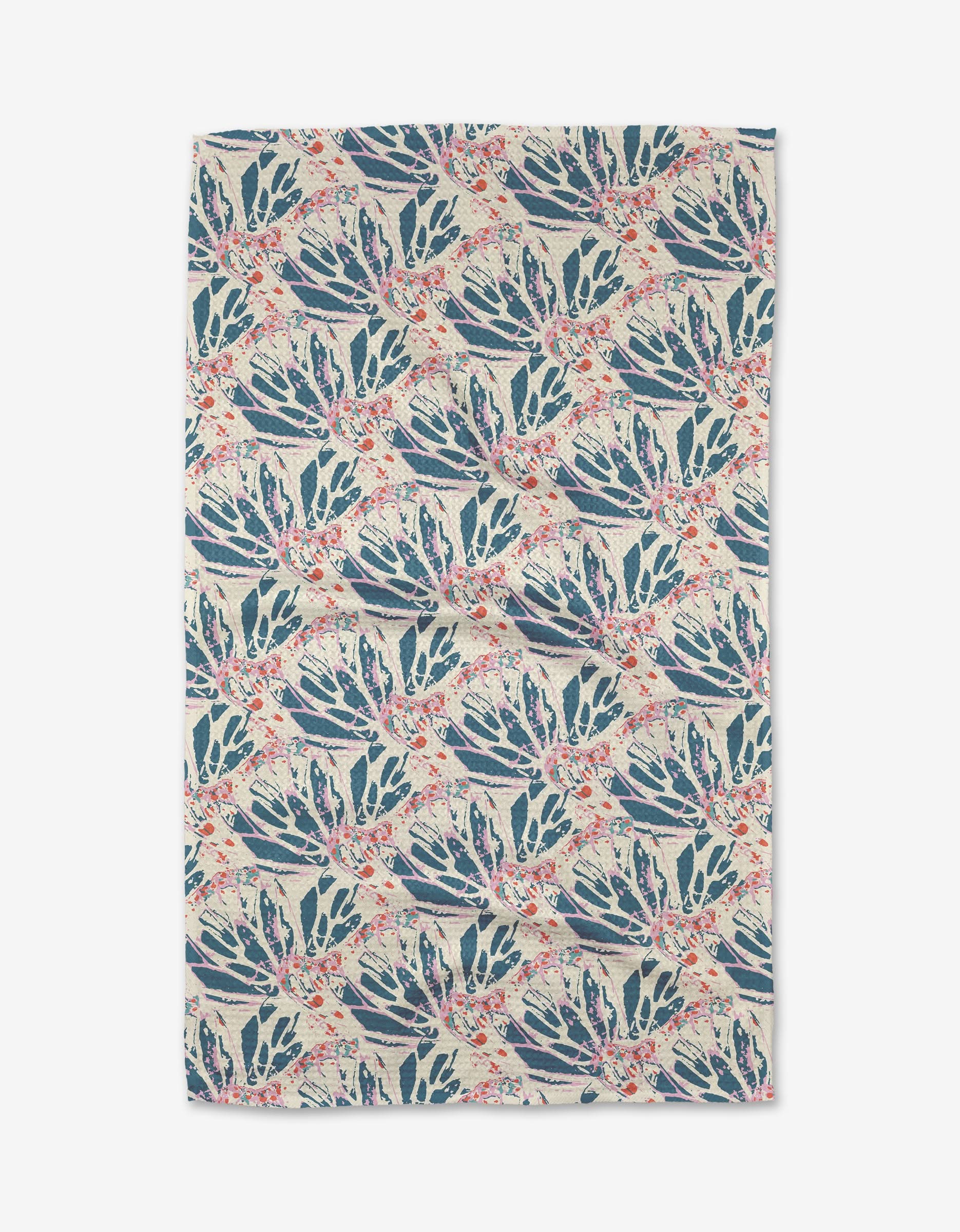 The Kaleidoscope Dream Tea Towel by Rebecca Woolbright features ultra-absorbent Geoweave fabric and a hand-painted, symmetrical pattern of blue and green botanical leaves with red accents on beige.