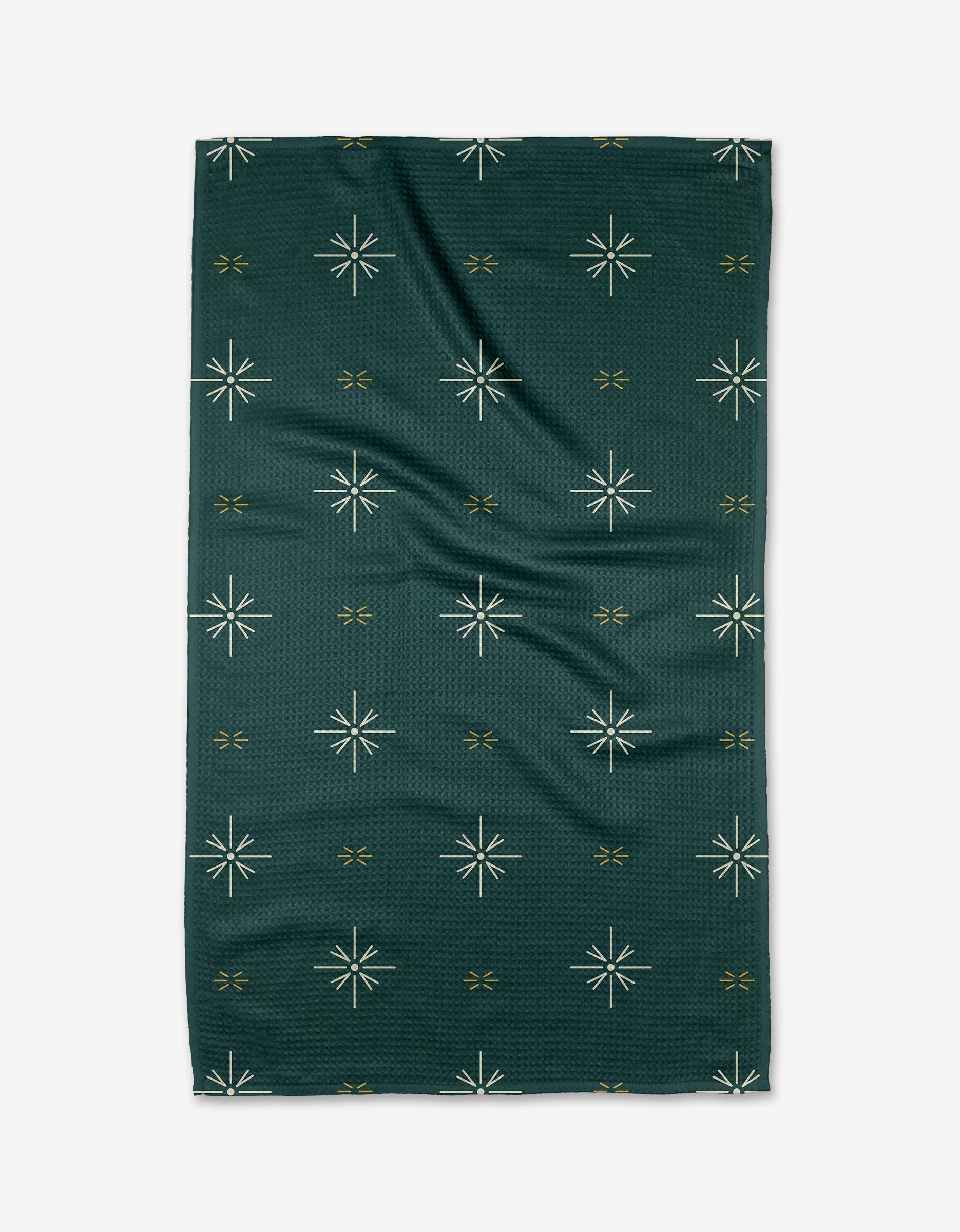The Marine Navigation tea towel by Twig + Spark is a dark green rectangle with white starbursts and small gold x-shapes on a textured background. Quick-drying, it’s shown flat with slight creases.