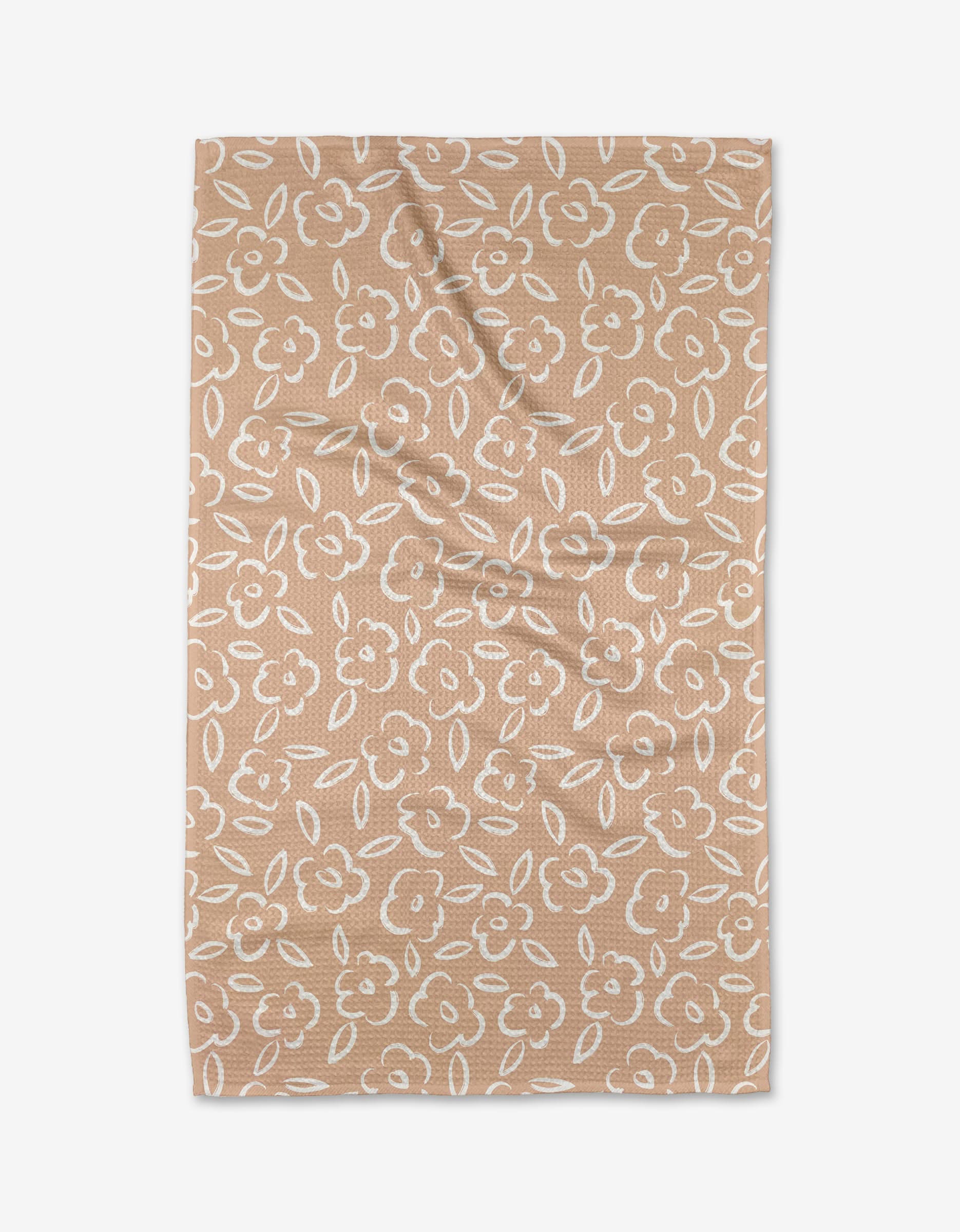 The Painted Bloom kitchen towel by Hufton Studio features a tan color with a white floral and leaf pattern all over. Displayed flat on a white background, the towel shows some light folds and is crafted from recycled materials.