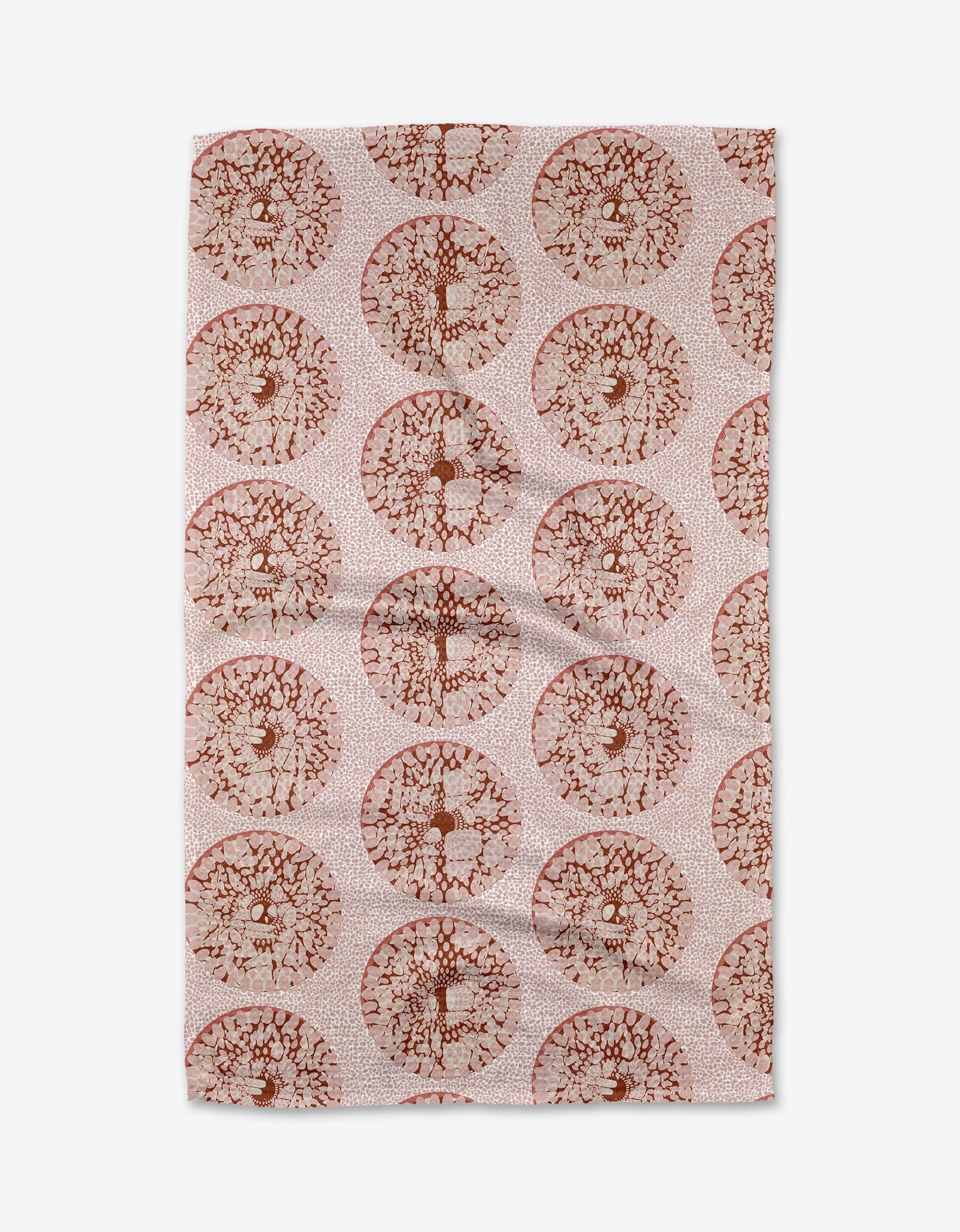 The Dabney Lee Pebbles tea towel is rectangular and pink, featuring a repeating pattern of circular, tree-like designs in brown and red shades, evenly spaced on slightly wrinkled fabric.