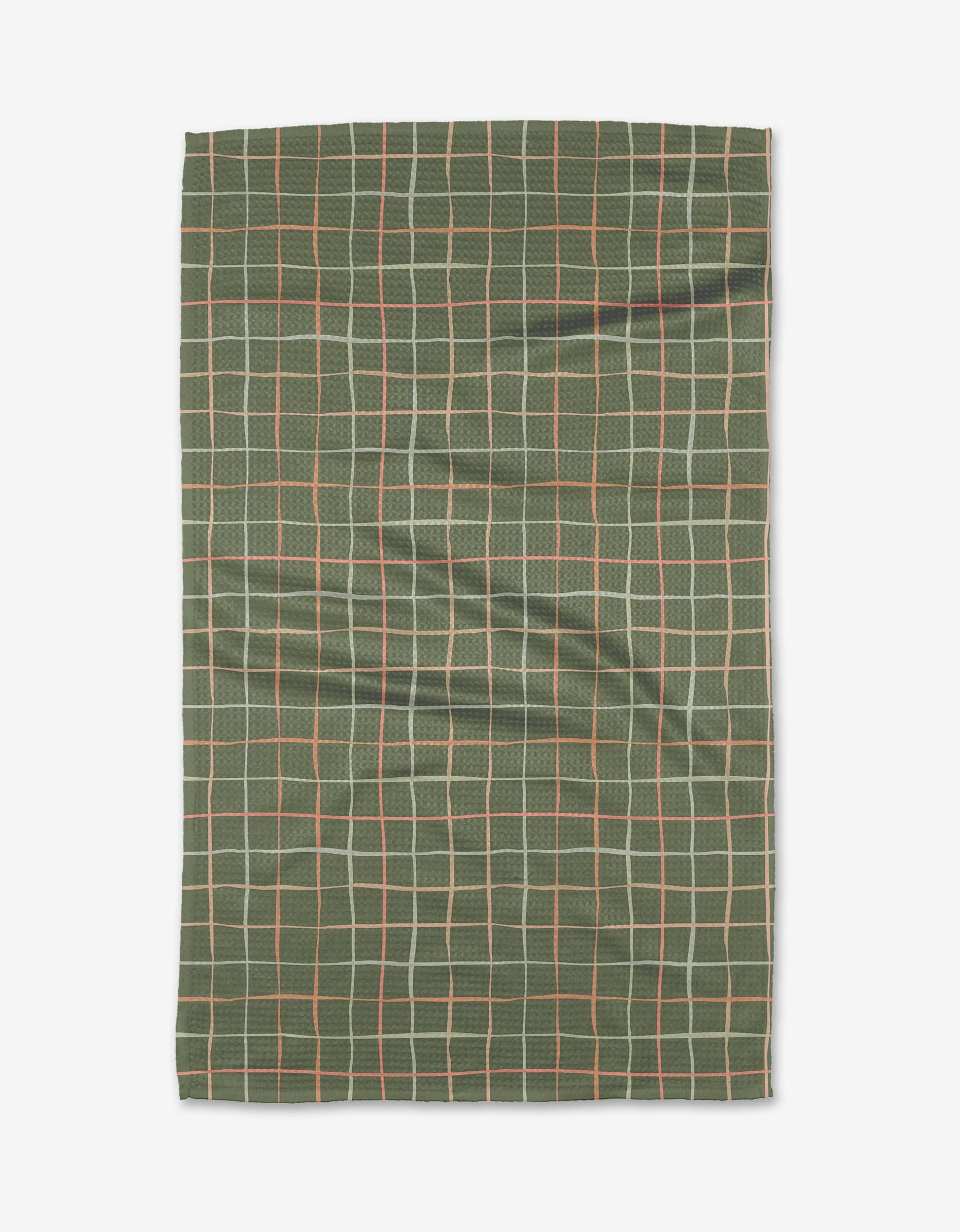 The Picnic napkin by Anee Shah is a green, recycled cloth featuring a grid pattern with thin white, beige, and orange lines on a plain white background. The fabric shows slight wrinkles for a relaxed look.