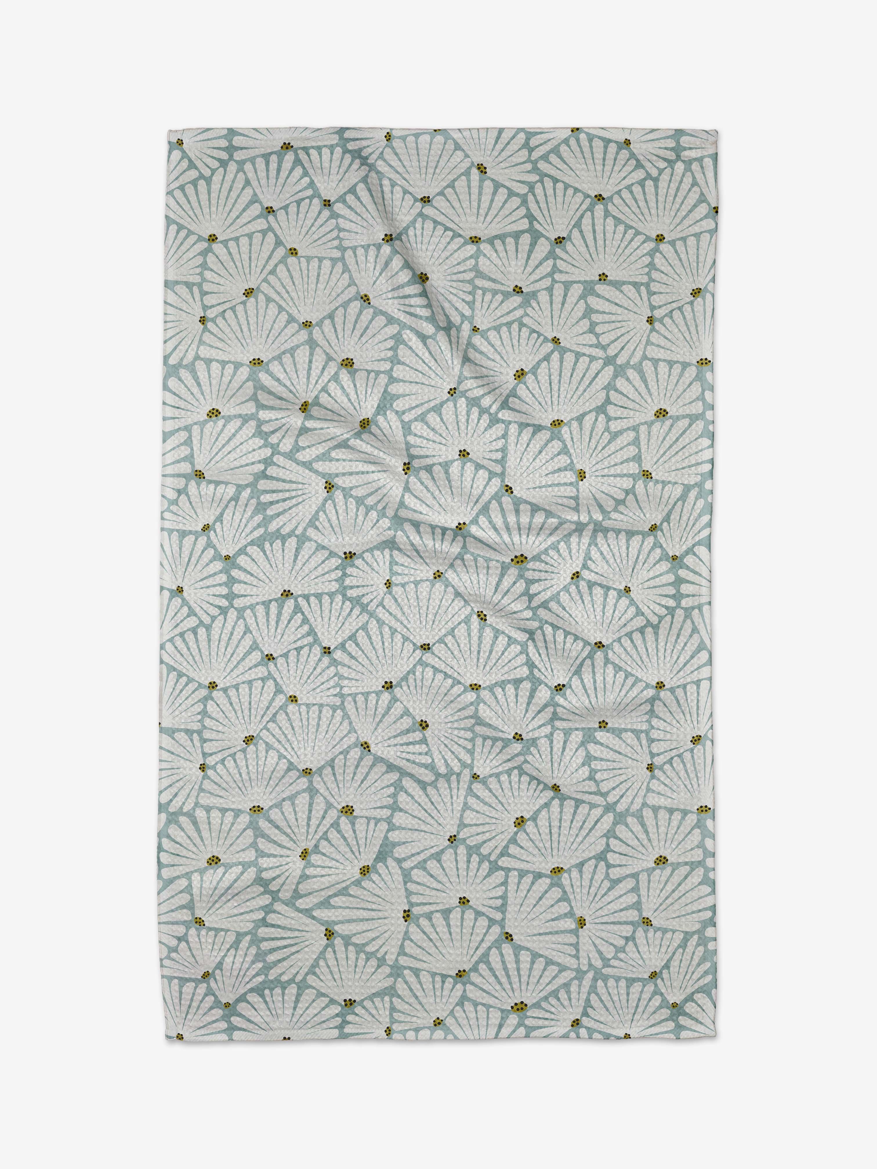 The Solie Teal Tea Towel by Amy MacCready features a repeating pattern of light blue and white fan-shaped leaves with small yellow accents, crafted from Geoweave fabric on a white background for a soft, airy look.