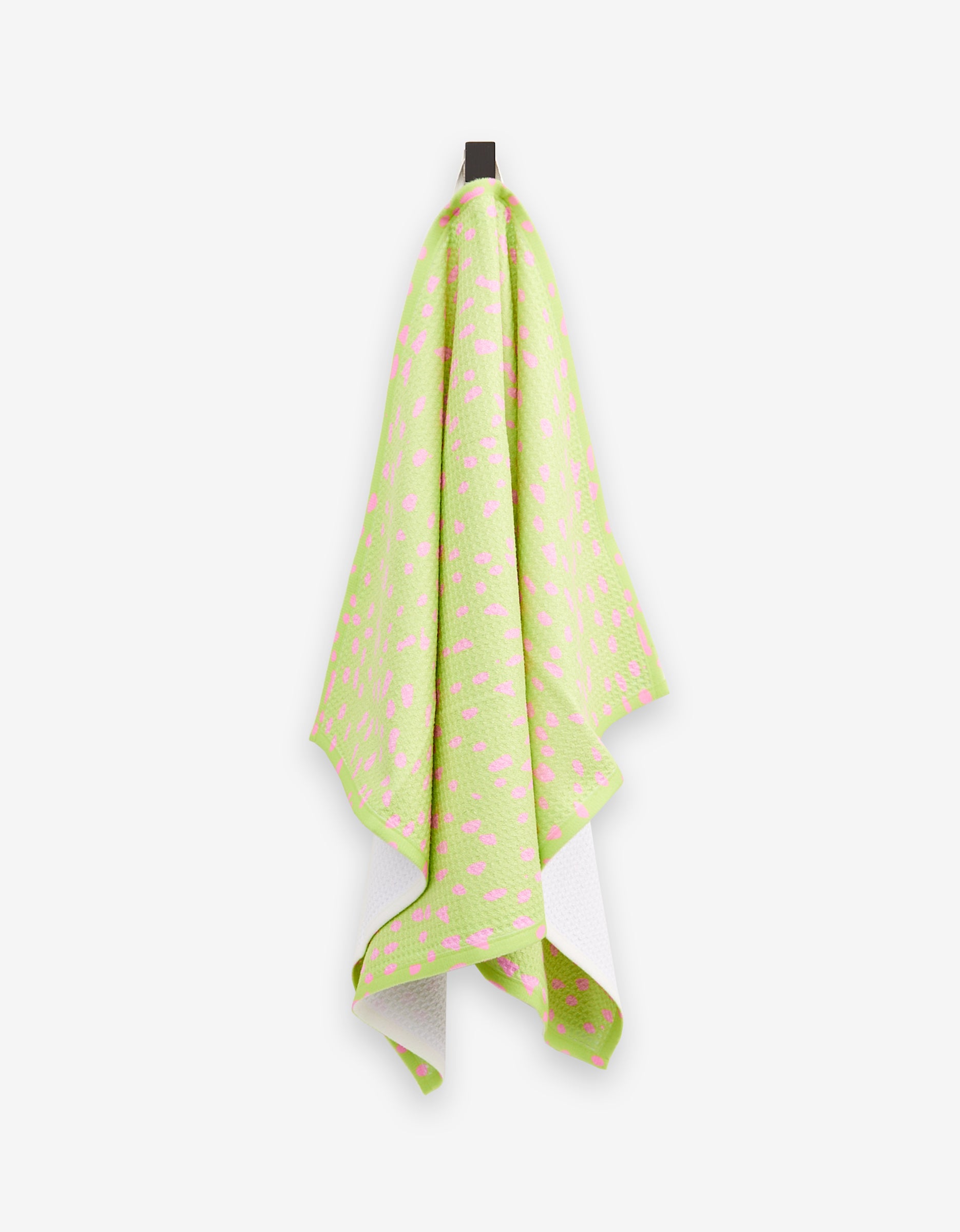The GEOMETRY Speckle Green tea towel, featuring a pink geometric pattern and soft Geoweave fabric, hangs on a hook against a white background. Its slightly curved edges add a modern accent to your kitchen.