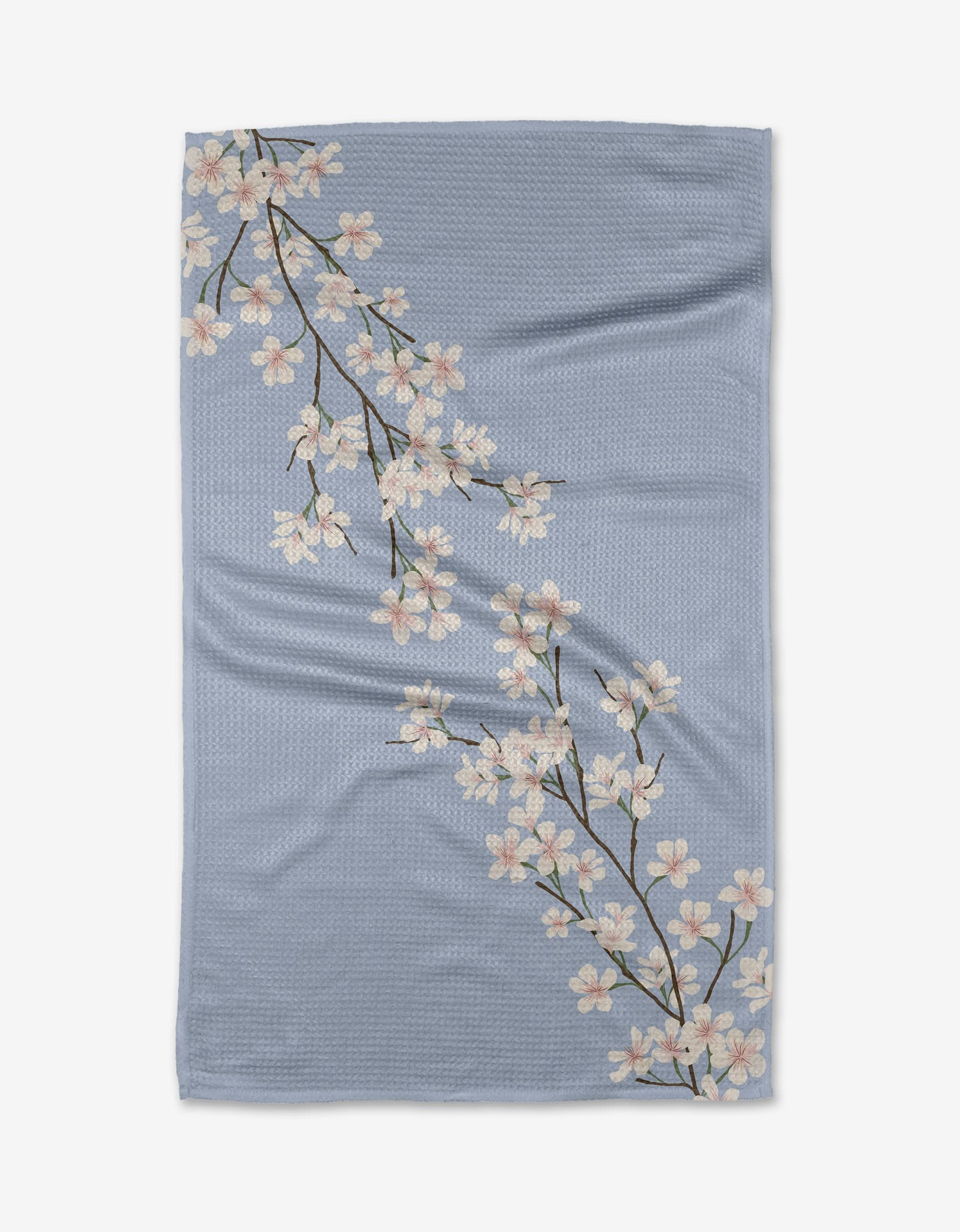 The Eve by Becki Owens is a light blue Geoweave™ blanket with two white cherry blossom branches, green leaves, and brown stems, crafted from recycled materials.