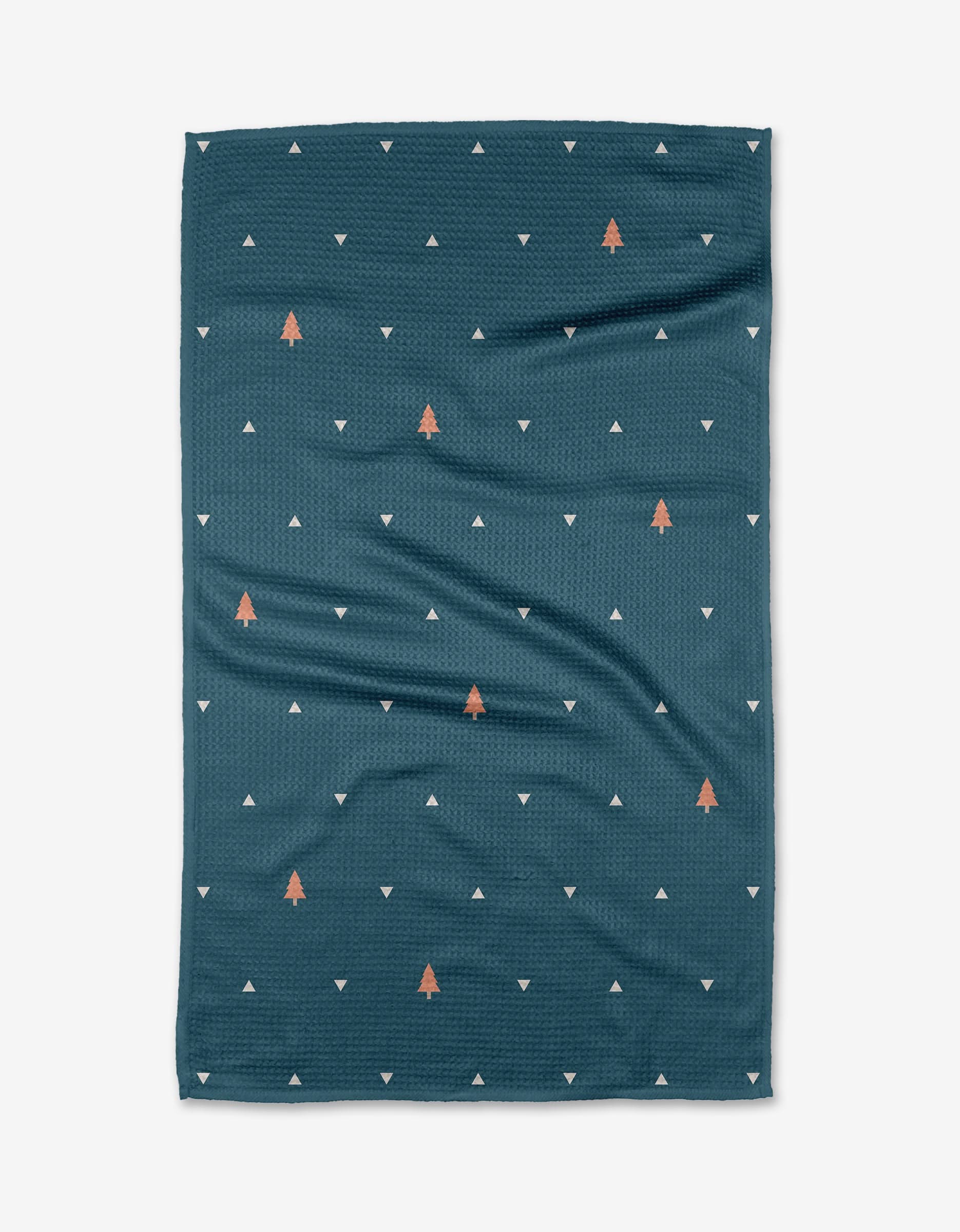The Twig + Spark Tree Dots tea towel, made from Geoweave fabric, features a dark teal background with white triangles and orange tree shapes, shown laid flat on a white surface.