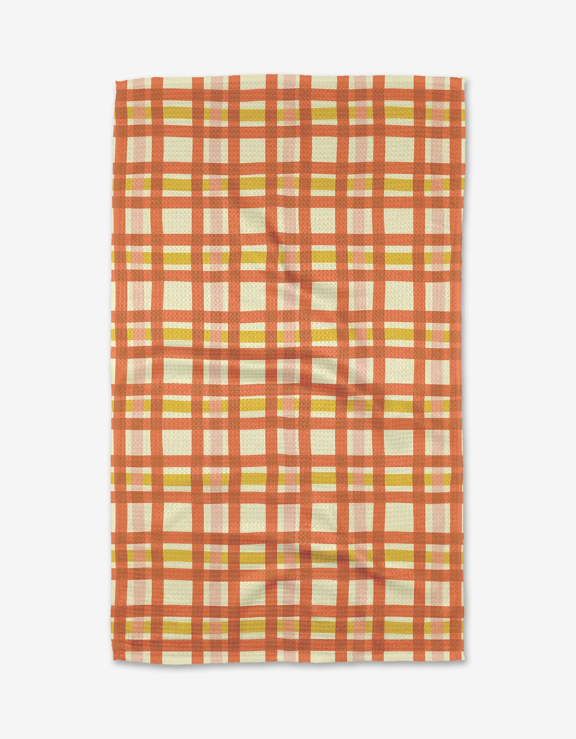 The Wonky Plaid tea towel by Kelsey Weigl features a red, orange, and yellow plaid on cream, made from recycled materials and displayed flat on a white surface.