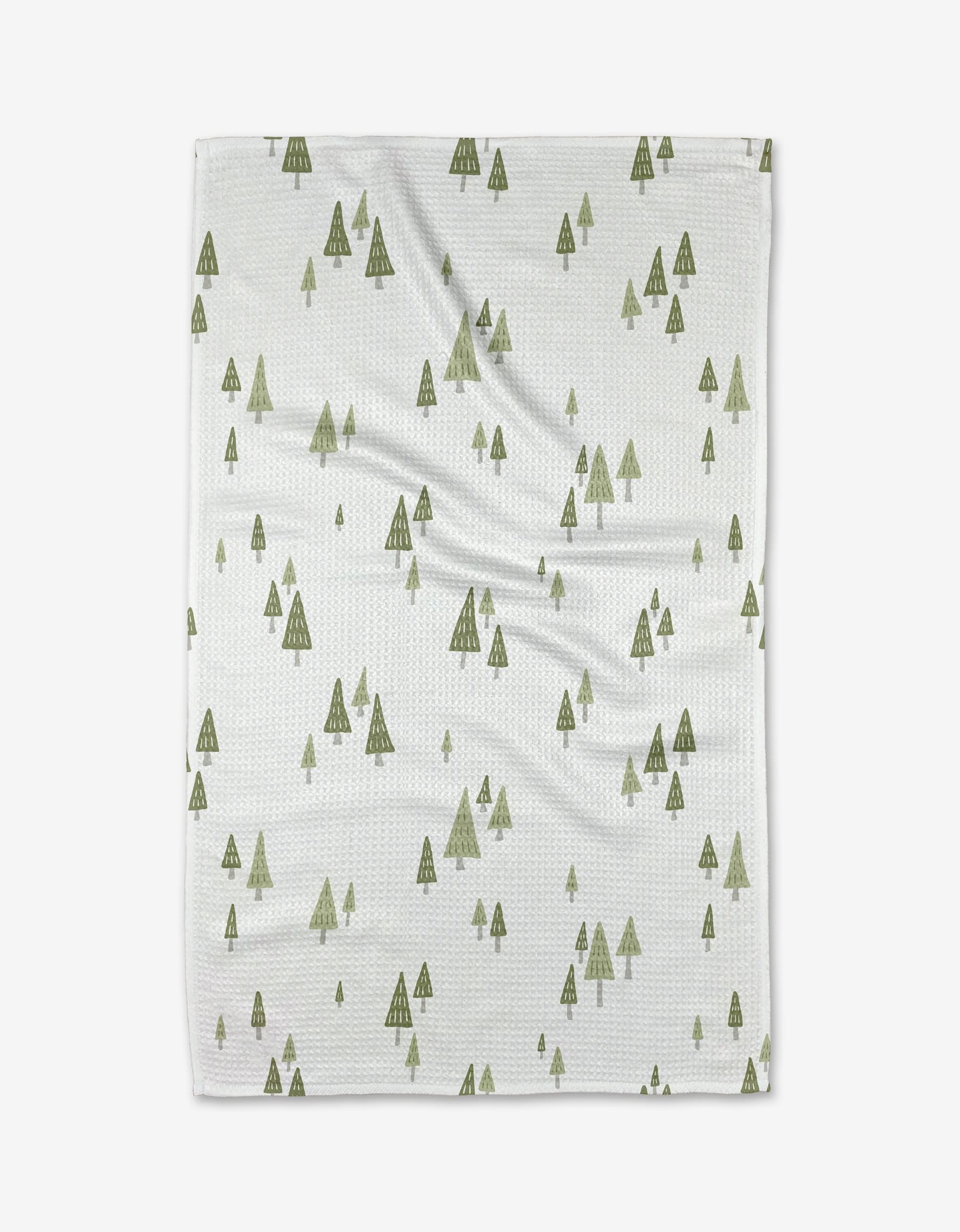The Woodruff tea towel by Amy MacCready features a repeating pattern of small, green pine trees on white Geoweave fabric, shown flat against a plain white background.