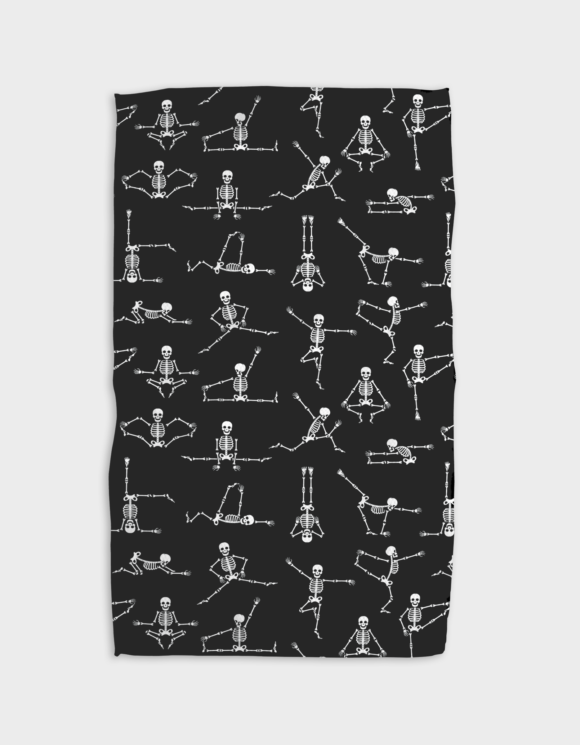 The GEOMETRY Yoga Bones blanket is black, made from recycled materials, and features a repeating pattern of white skeletons in various yoga and seated poses.