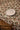 A white plate, fork, knife, and spoon are set on a table with a patterned tablecloth featuring oranges and green leaves; a wooden chair is placed beside the table.