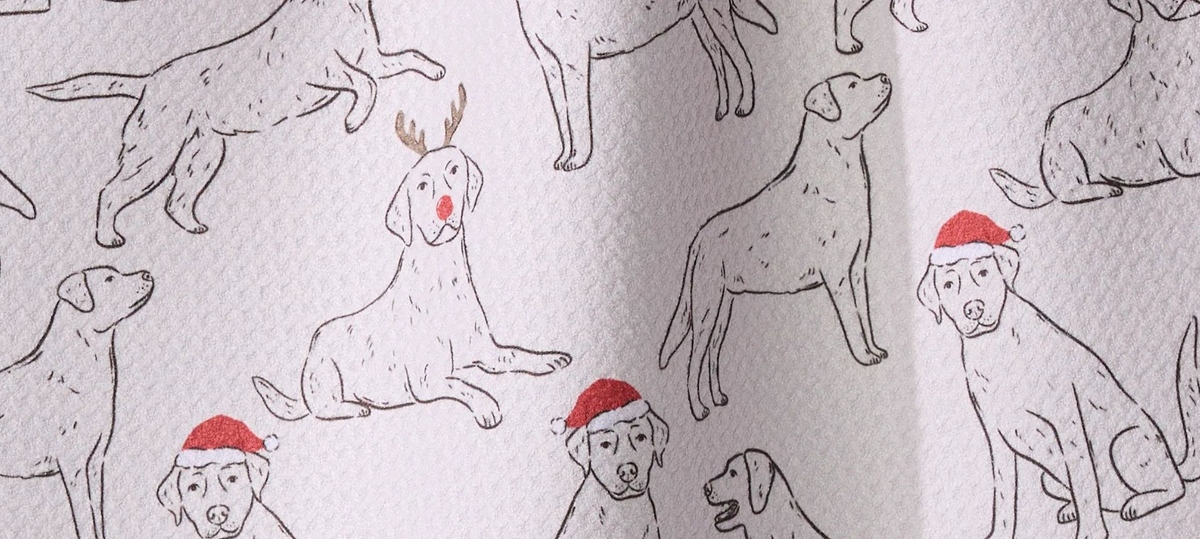 A pattern of line-drawn Labrador retrievers, some wearing red Santa hats or reindeer antlers with a red nose.