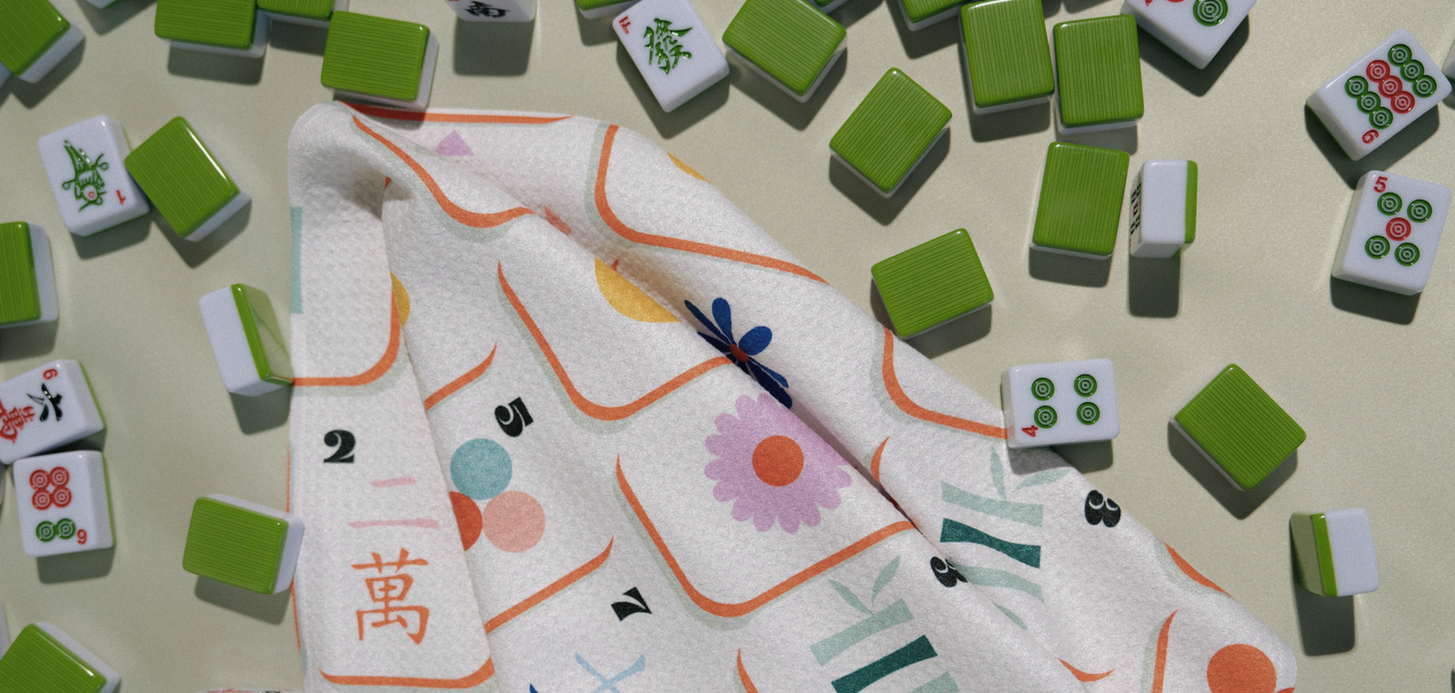 A colorful towel with oval patterns and the words DOT BAM CRAK hangs over a wooden chair next to a table. Green plant leaves are visible in the background.