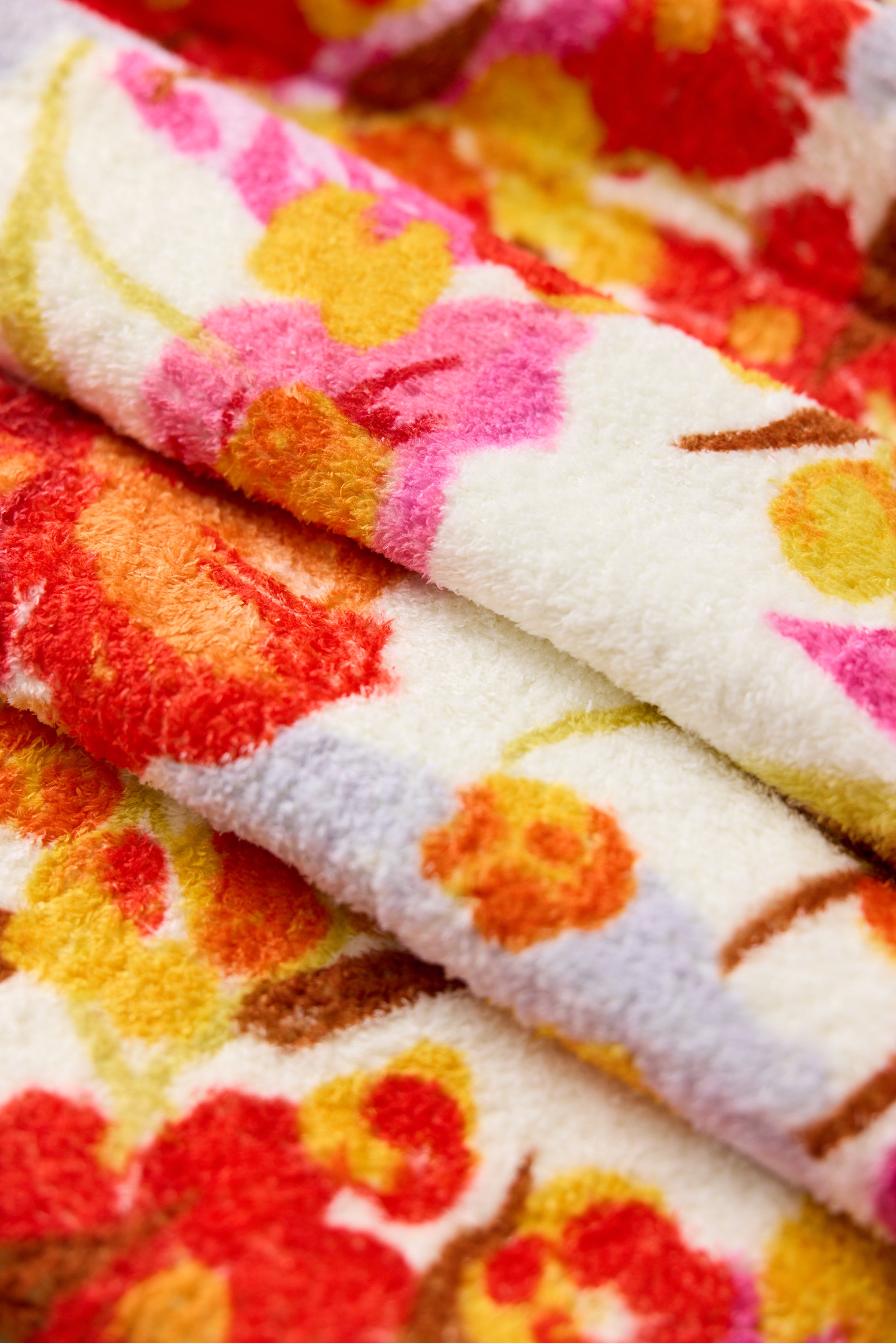 Close-up of soft, fluffy towels with a colorful floral pattern in shades of red, pink, yellow, and orange on a white background.