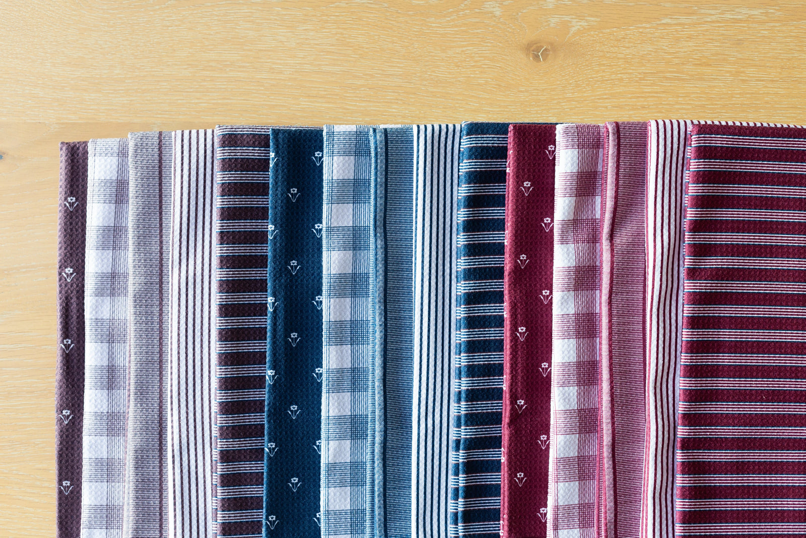 A row of folded dress shirts in various patterns and colors, including stripes and checks, arranged neatly on a light wooden surface.