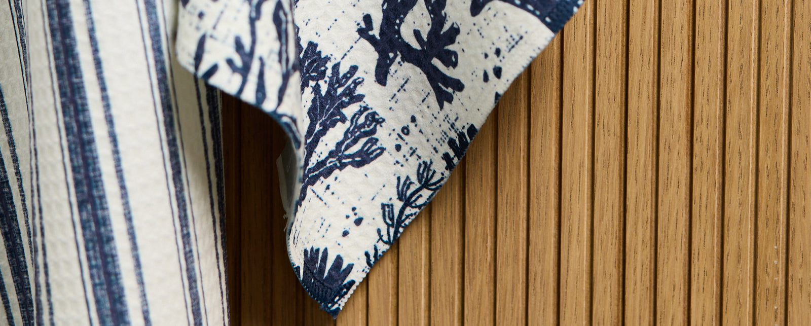 A close-up of a blue and white patterned fabric with botanical designs, draped in front of a vertical wooden slat wall.