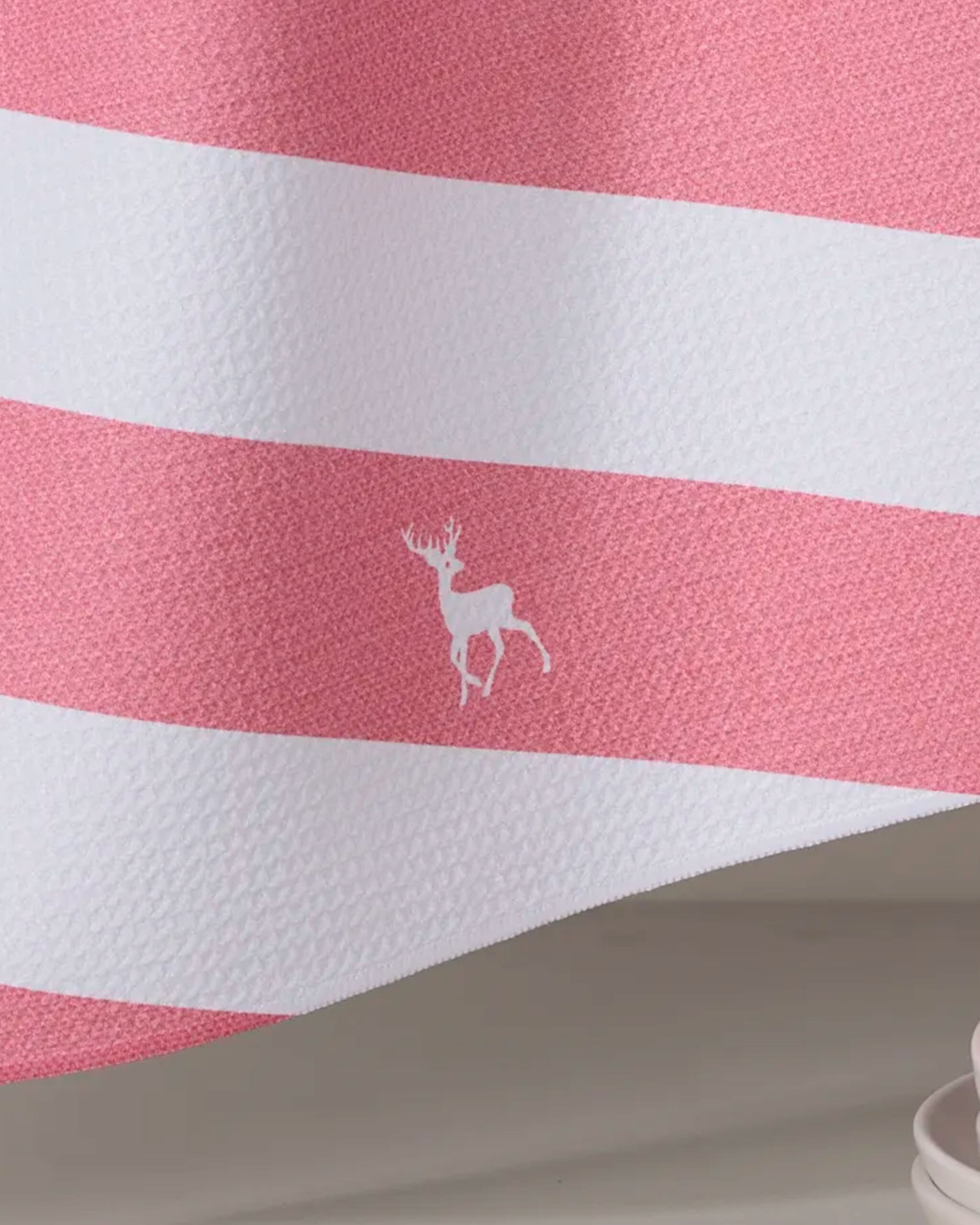 The Geometry Reindeer Run tea towel features pink and white stripes with a small white reindeer silhouette centered on a pink stripe, crafted from recycled materials.