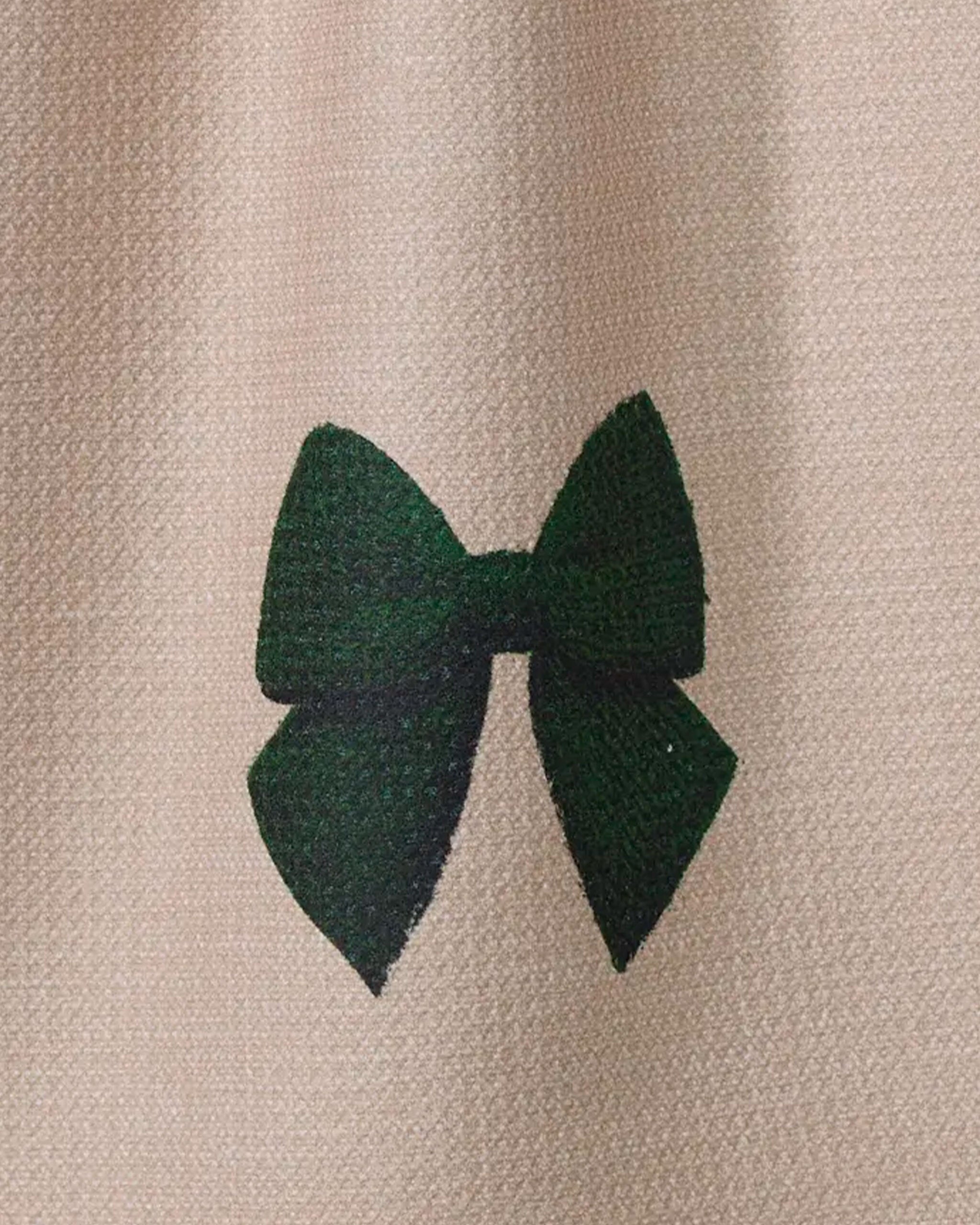 The Vireo tea towel by Geometry features a simple dark green bow print on textured beige fabric, offering both absorbency and eco-friendliness—an elegant, stylish addition to any kitchen.
