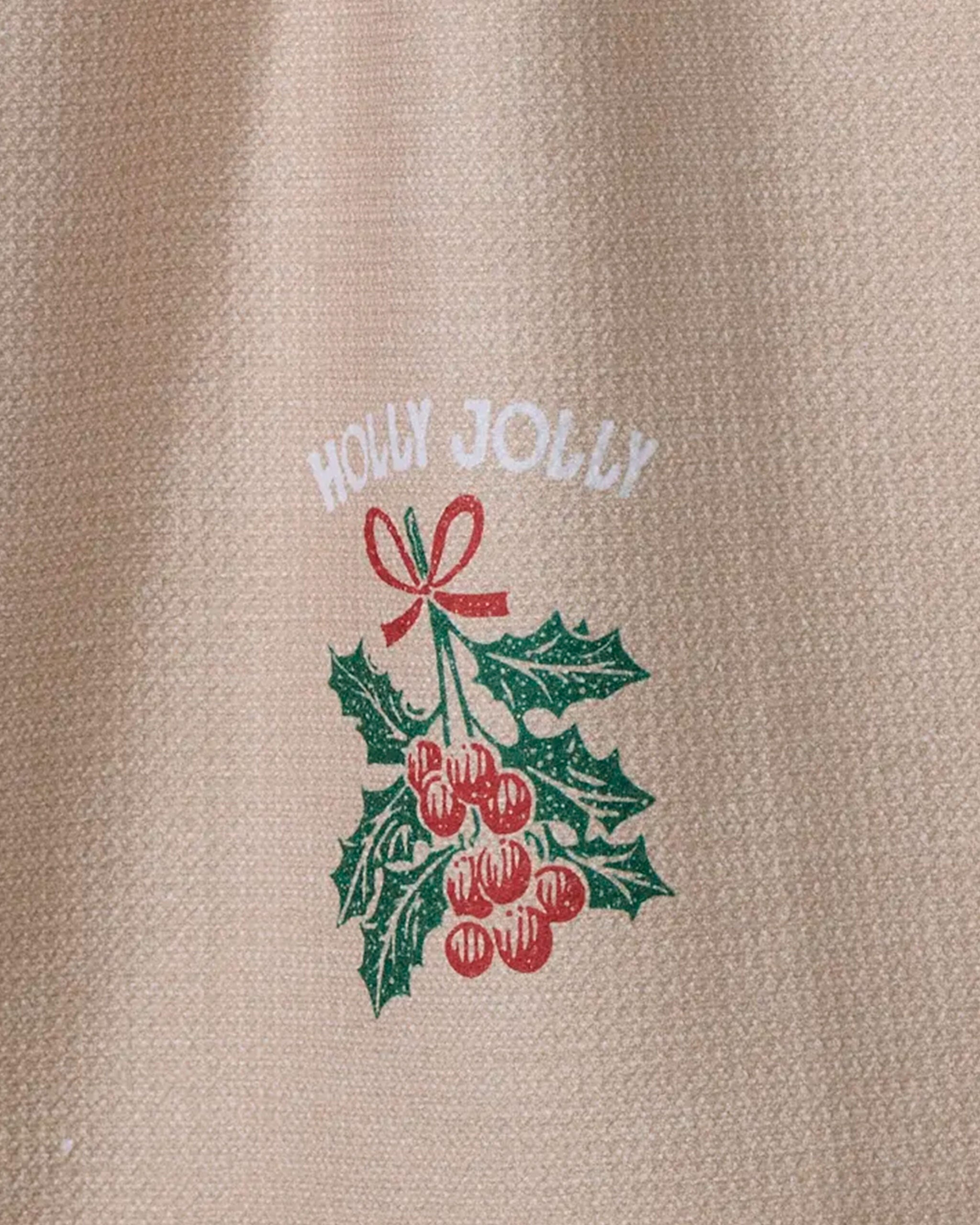 The "Merryberry" kitchen towel by Geometry is beige, features a holly and berry design tied with a bow, "HOLLY JOLLY" in white, and is made from recycled materials with a textured feel.