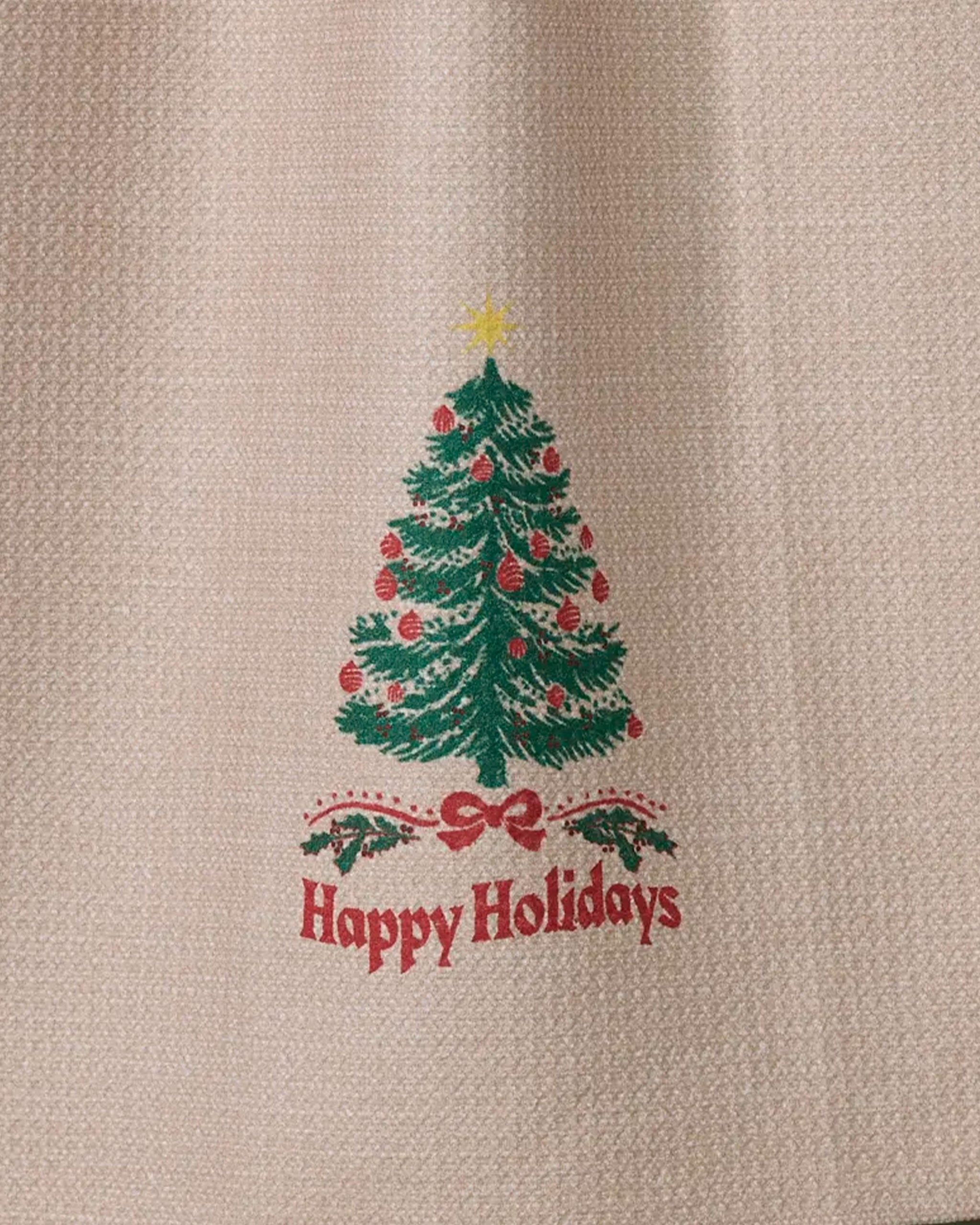 The Geometry Starwood kitchen towel features a green Christmas tree with red ornaments and a yellow star above the words "Happy Holidays" on textured beige fabric.