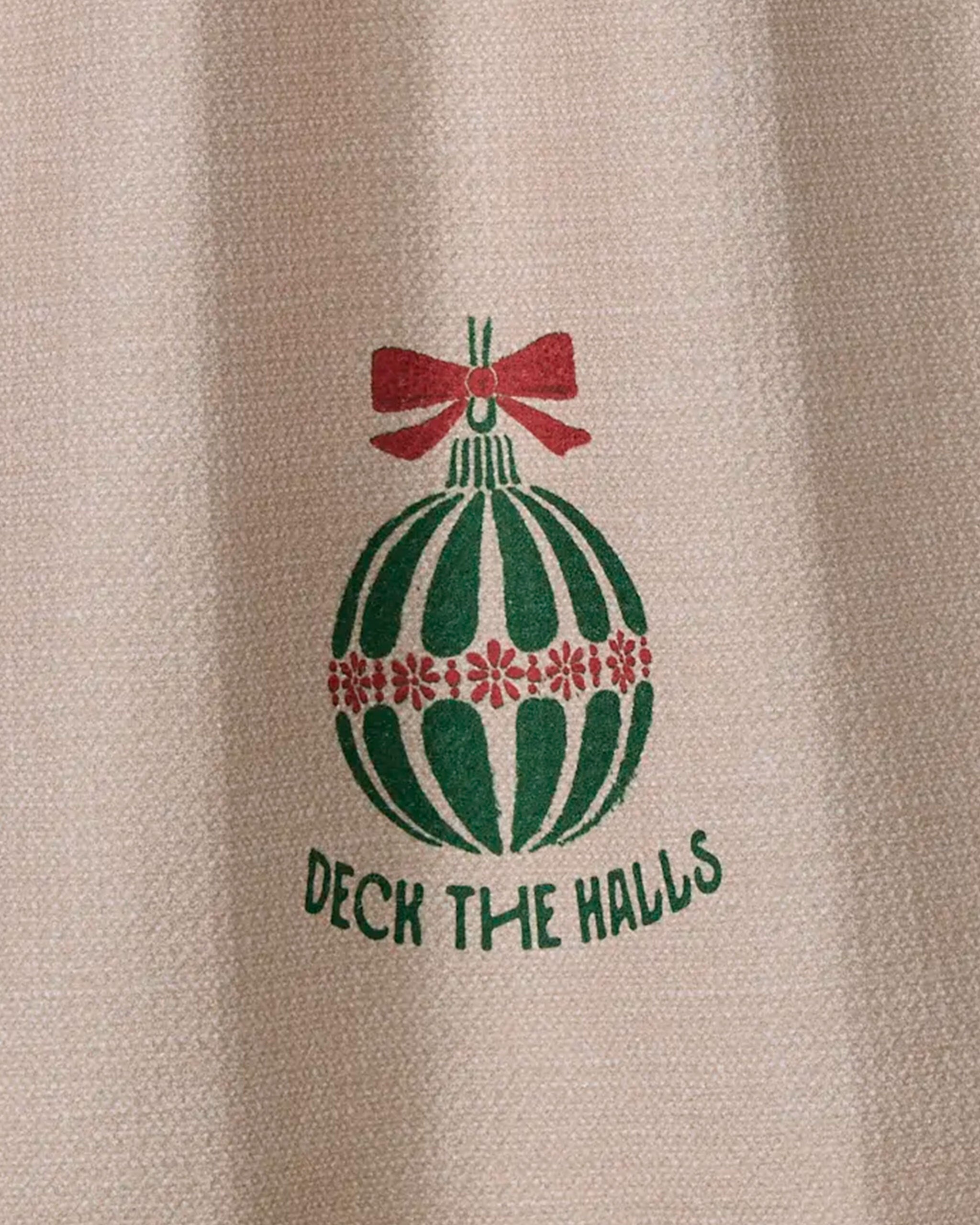 Festona by Geometry features a green Christmas ornament with a red bow and floral band on an ultra-absorbent tea towel, displaying "DECK THE HALLS" on beige textured fabric.