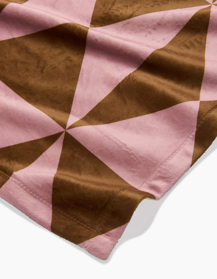 A close-up of Geometry’s Bronze blanket shows its soft, eco-friendly fabric with a geometric pinwheel pattern of alternating pink and brown triangles.