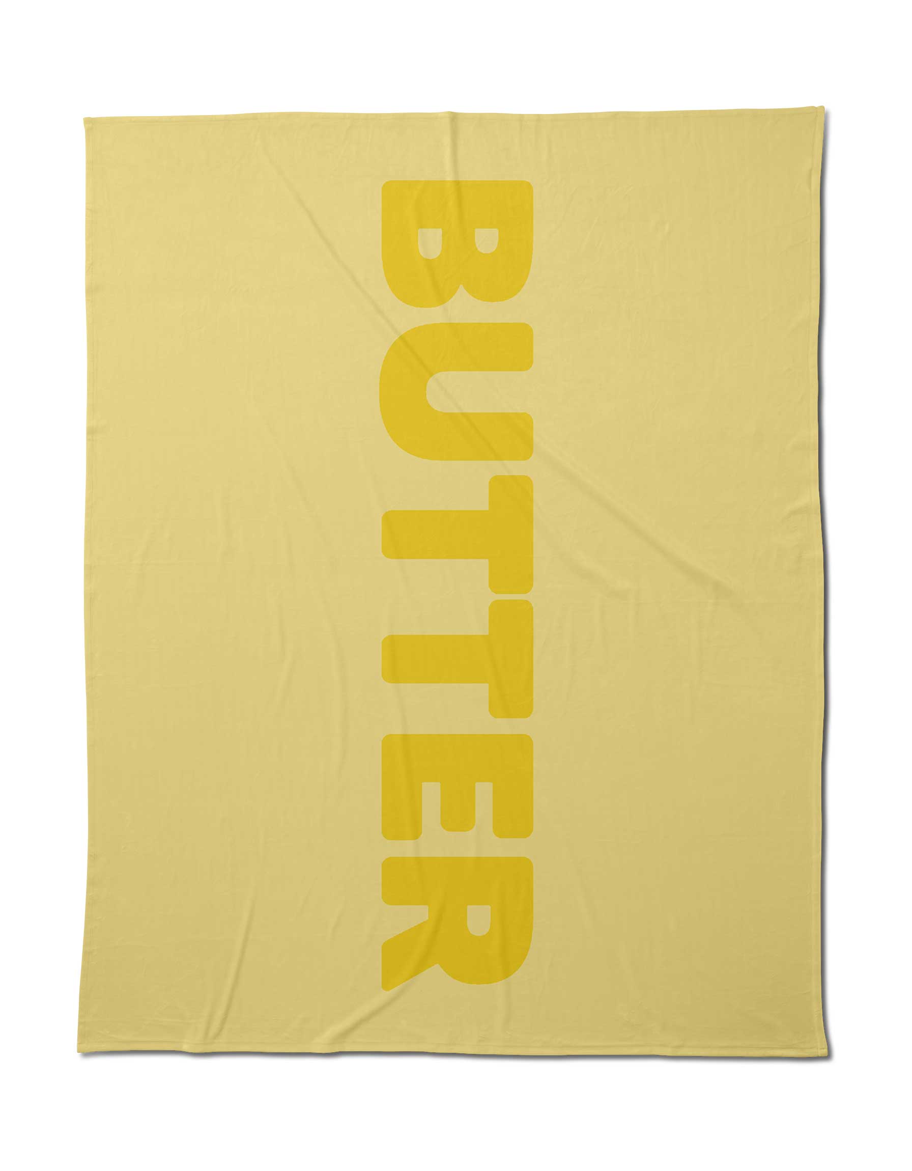 Geometry’s Butter Blanket in light yellow offers silky softness and features “BUTTER” in bold vertical yellow letters. Made from post-consumer recycled materials, it delivers a cozy, eco-friendly touch.