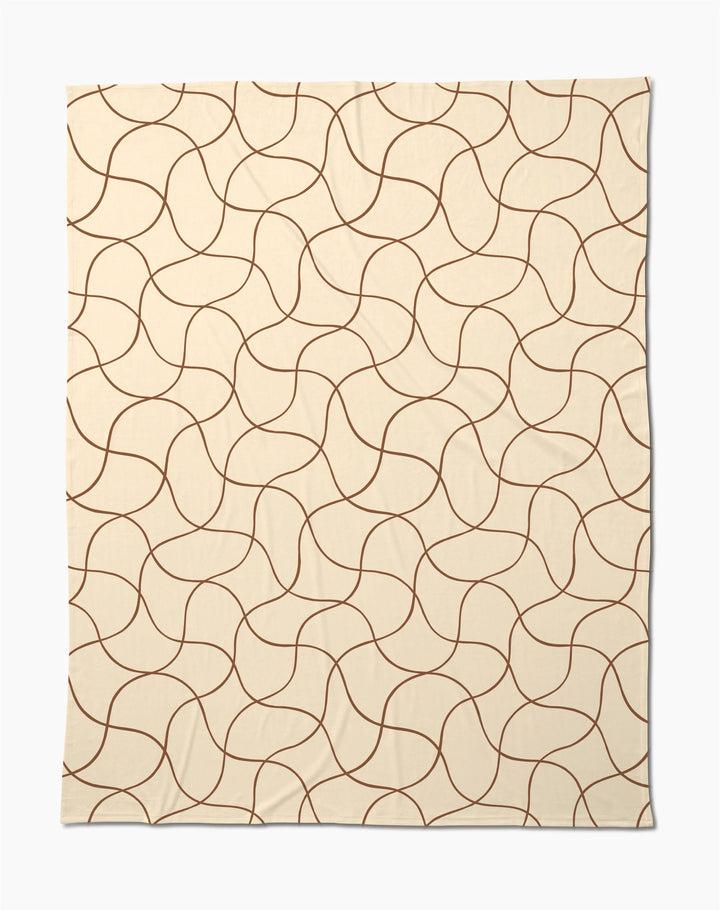 The Clarity throw by Geometry features a beige butter hue with abstract, wavy brown lines—a soft, cozy blanket perfect for relaxing evenings.