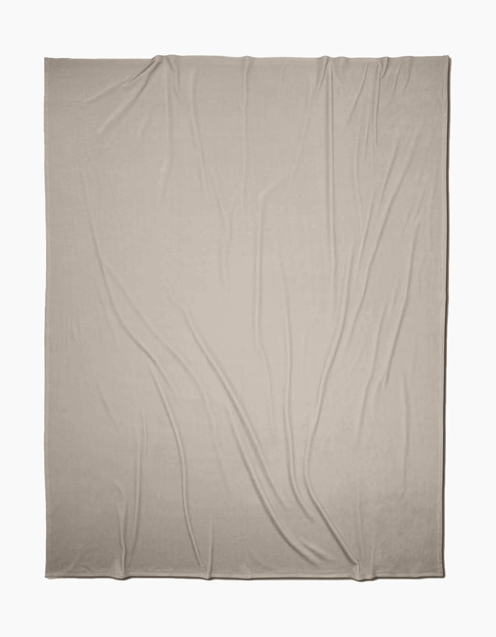 A GEOMETRY Desert Haze Butter Blanket, in light beige, is laid out flat with soft folds and wrinkles on a white background, highlighting its silky texture.