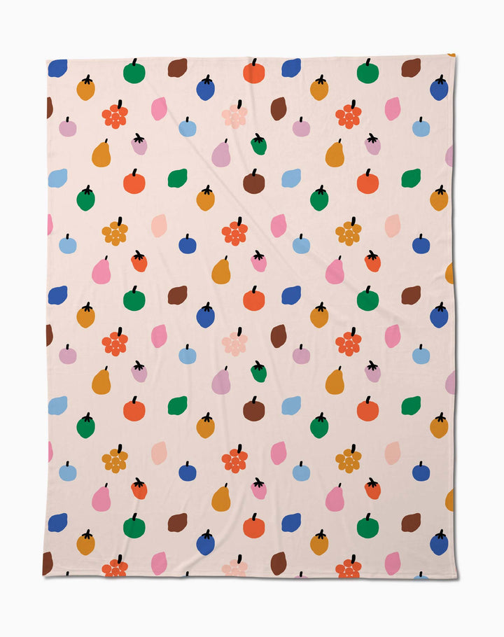 The Fruit Basket Butter Blanket by Jennifer Bouron is a beige, eco-friendly throw made from recycled materials, featuring a playful mix of fruit shapes, blobs, and flowers in vibrant colors.