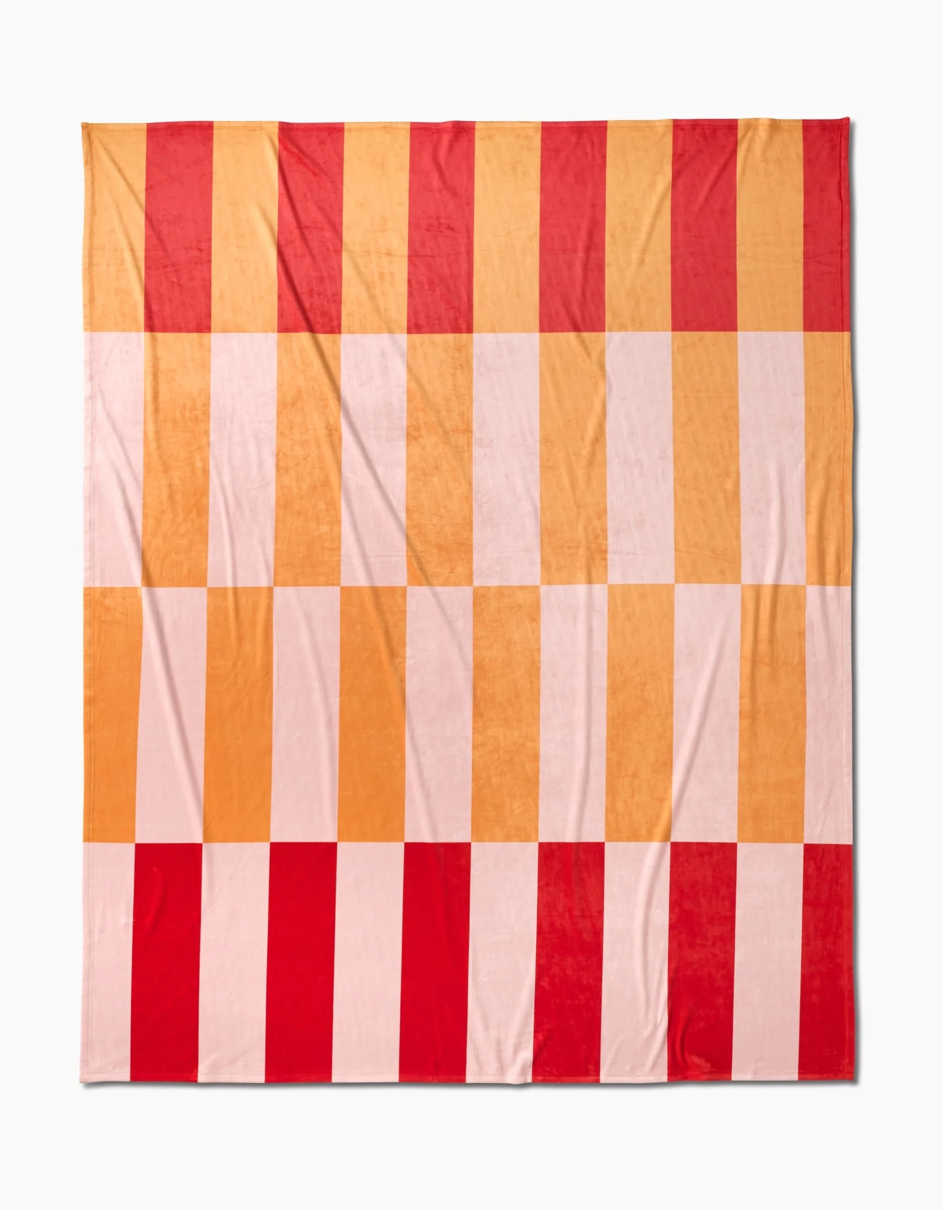 The Geometry Geometric Sunset Butter Blanket features a bold checkered pattern in red, orange, peach, and pink stripes. Made from recycled materials, its fabric offers silky softness with gentle folds and creases.