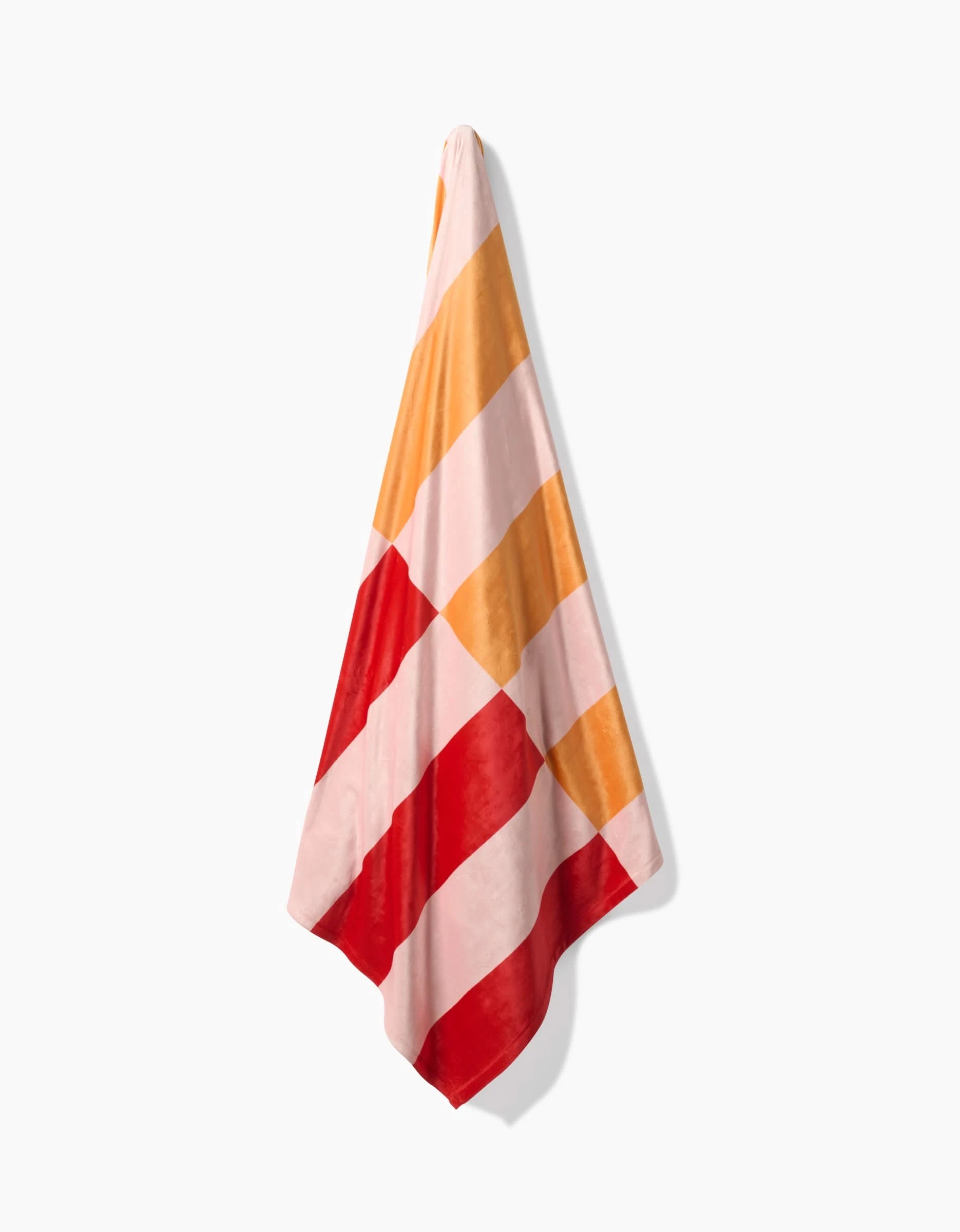 The Geometry Geometric Sunset towel, featuring silky softness and diagonal stripes in red, pink, and yellow tones, hangs against a plain white background.