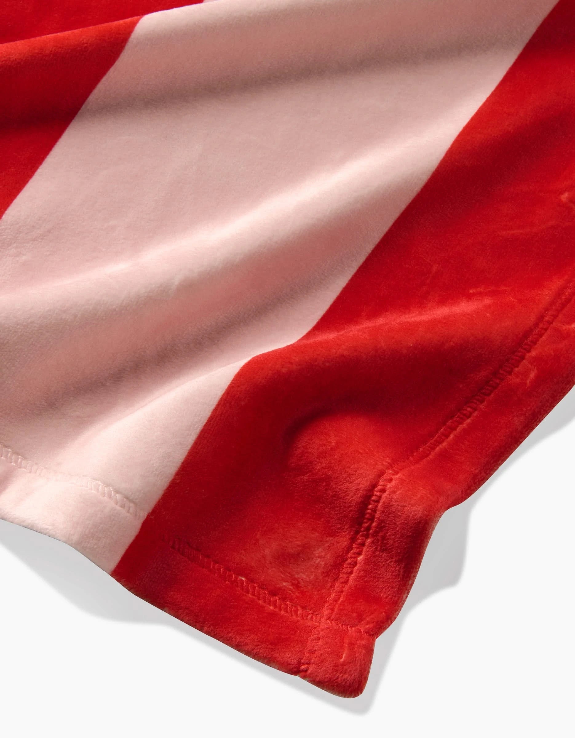 A close-up of Geometrys Geometric Sunset shows its soft, velvety fabric with wide red and light pink stripes made from recycled materials, highlighting the texture and seam along the edge.
