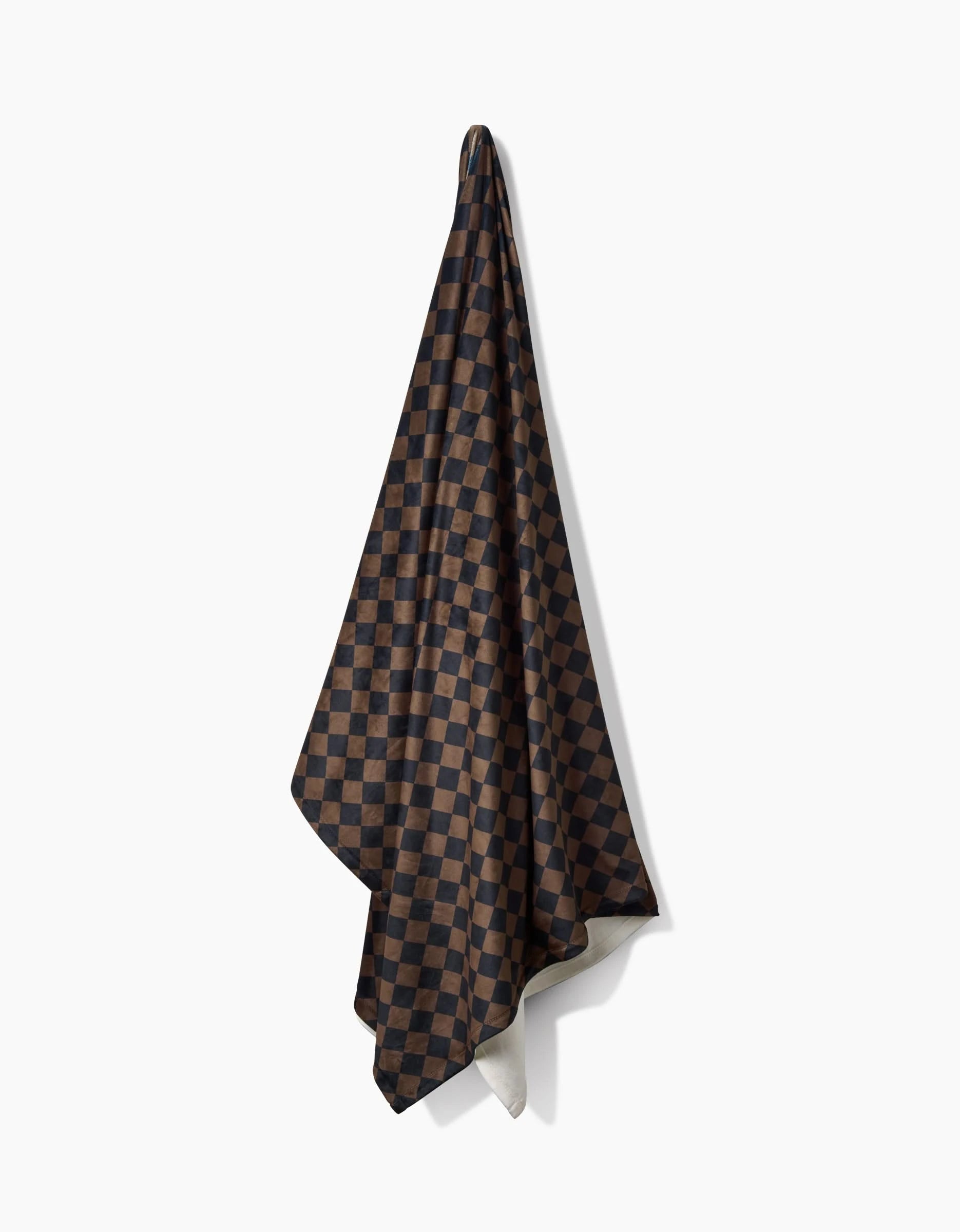 The Geometry Gridlock towel, featuring a dark brown and black checkered pattern, hangs on a single hook against a white background.