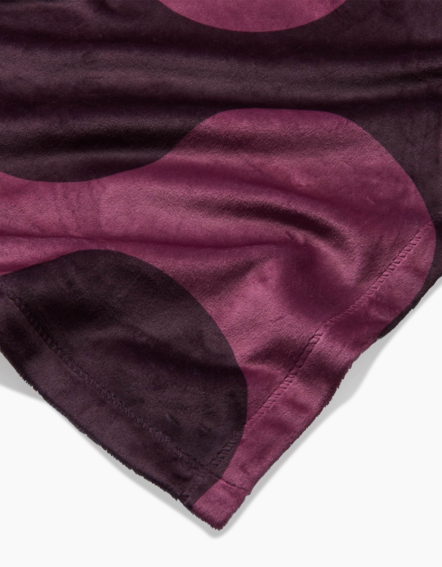 A close-up of the Geometry “Groove With Me” Butter Blanket features a dark purple and magenta circular pattern, stitched edges, and a velvety texture for ultimate silky softness.