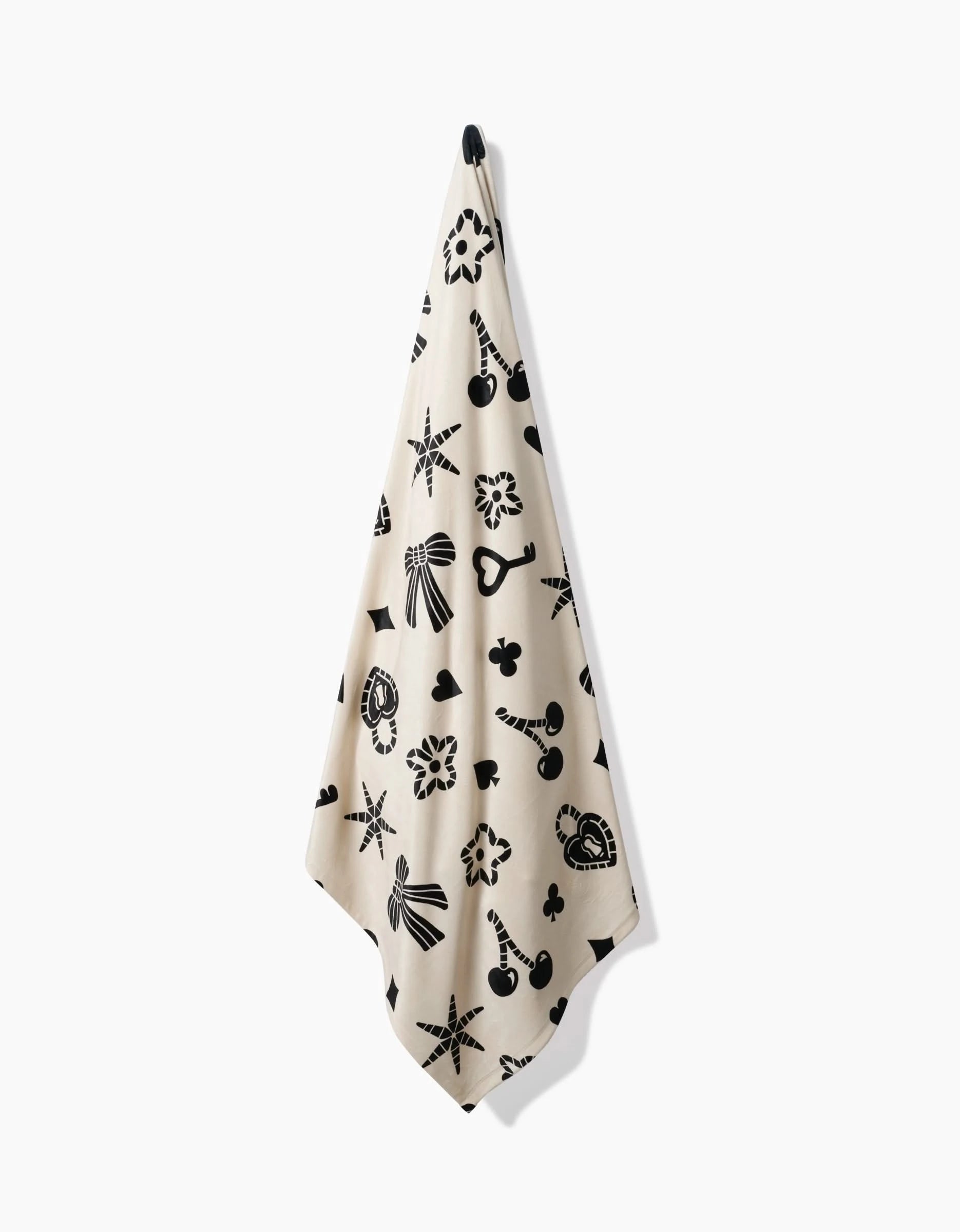 A Heart Locket towel by Geometry with beige tones and black heart locket designs hangs from a hook against a white background, offering silky softness for a luxurious feel.