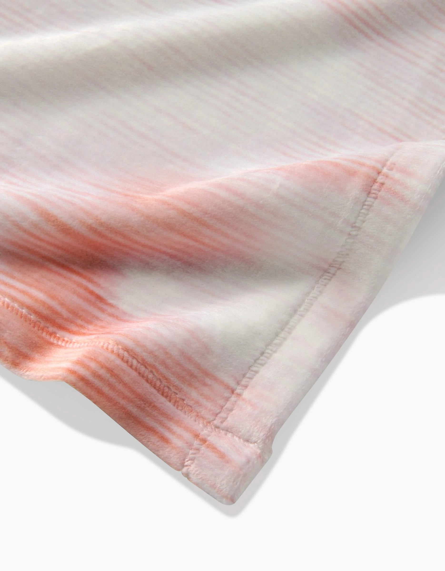 Close-up of Geometrys In the Clouds Butter Blanket, showcasing its silky soft fabric with a pink and white tie-dye gradient. The image zooms in on the stitched edge, highlighting fine details and luxurious texture.