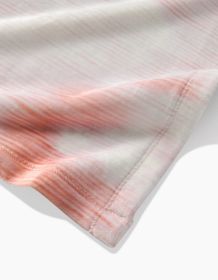 Close-up of Geometrys In the Clouds Butter Blanket, showcasing its silky soft fabric with a pink and white tie-dye gradient. The image zooms in on the stitched edge, highlighting fine details and luxurious texture.