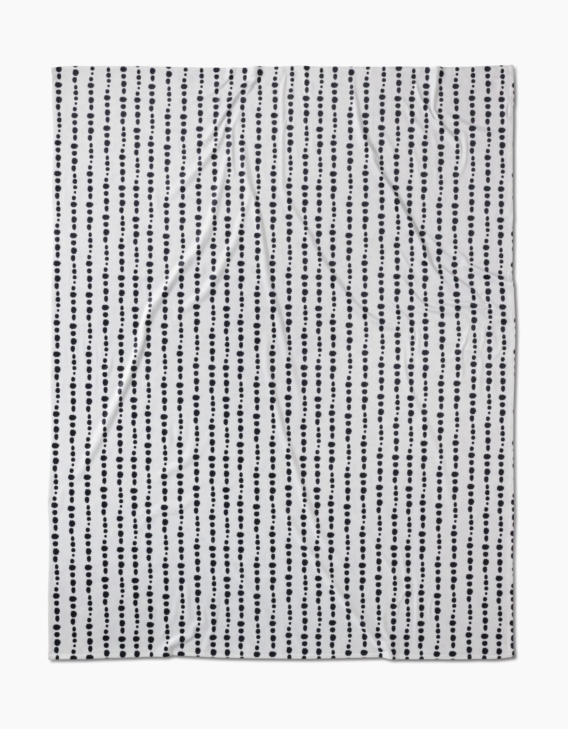 The Geometry Ink Dots Butter Blanket features evenly spaced vertical rows of small black dots on white, crafted from recycled materials with a subtly wrinkled texture.