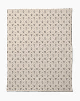 The Inked Bloom by Cole Strem is an eco-friendly, beige blanket with a simple, repeating black floral motif. Made from recycled materials, it appears soft with subtle natural wrinkles.