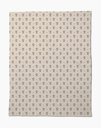 The Inked Bloom by Cole Strem is an eco-friendly, beige blanket with a simple, repeating black floral motif. Made from recycled materials, it appears soft with subtle natural wrinkles.