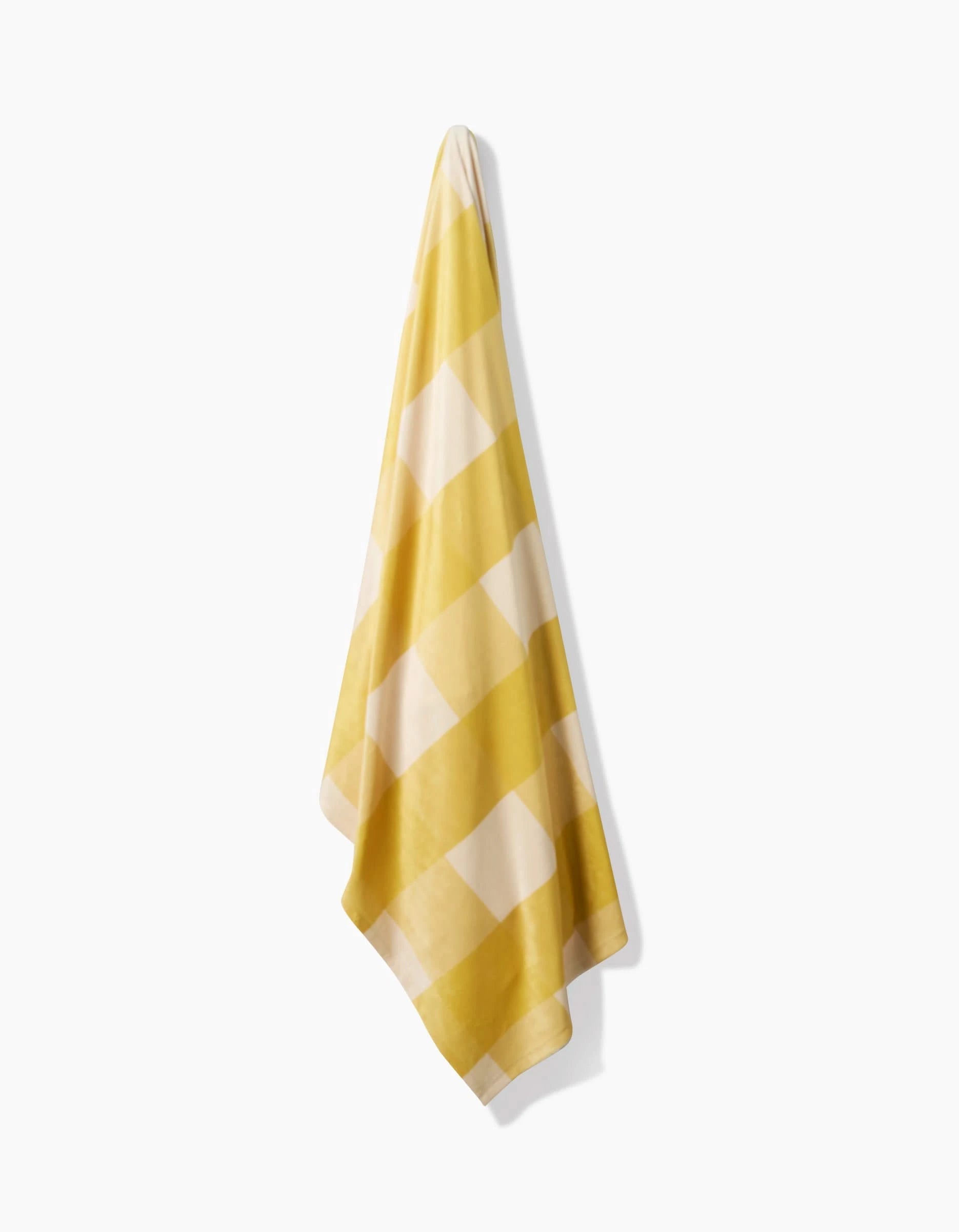 The Lemonade Gingham towel by Geometry, featuring a yellow and white checkered pattern, hangs on a hook against a plain white background.