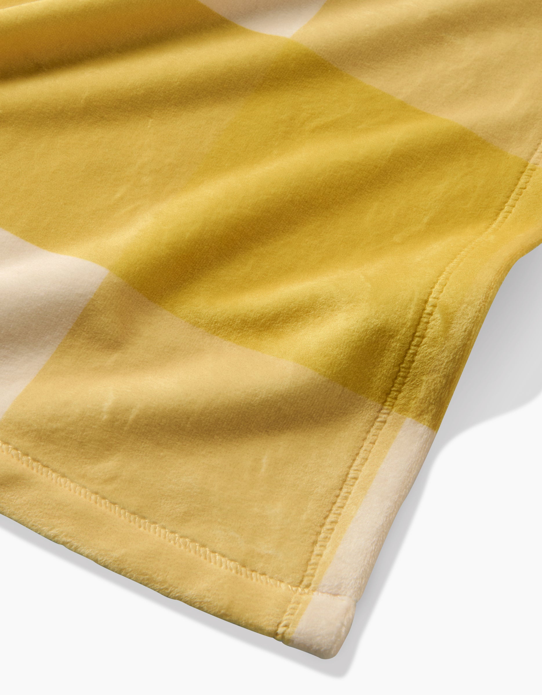 A close-up of Geometrys Lemonade Gingham Butter Blanket showcases a yellow and beige large checkered pattern, stitched edges, and subtle folds in the eco-friendly material.