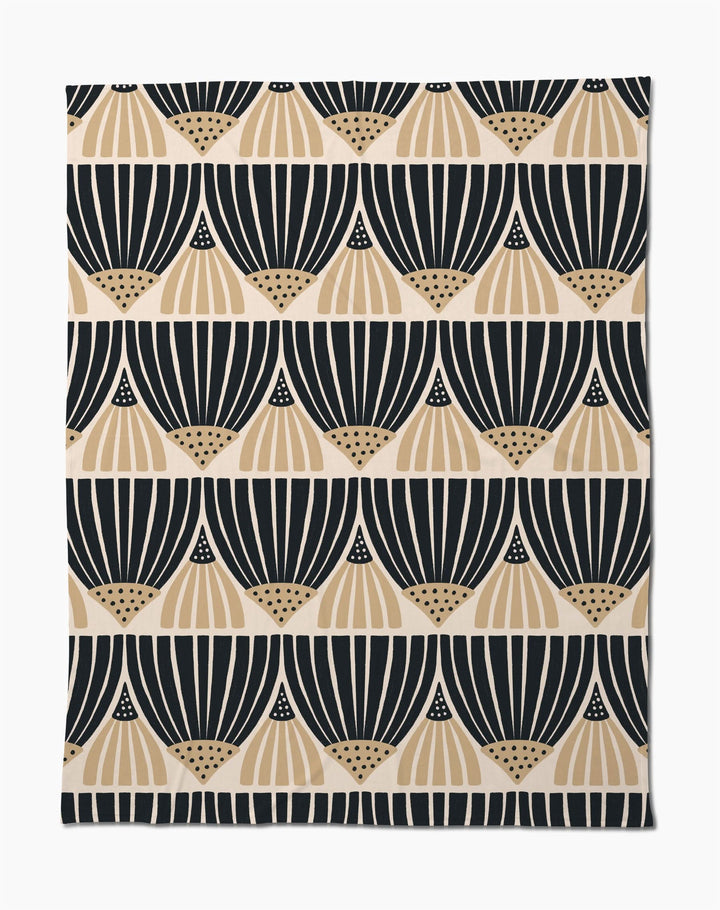 The Letitia Dark Butter Blanket by Amy MacCready features black and tan geometric fan patterns on white, arranged in horizontal rows. Made from eco-friendly recycled materials, it offers a modern, minimalist style.