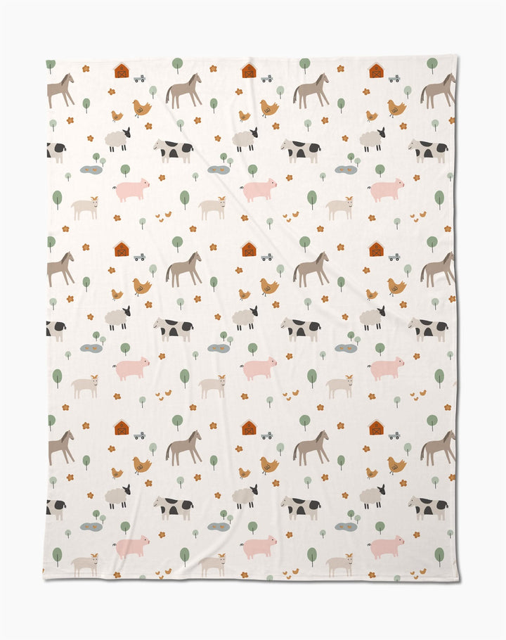 The Coit Creative Light Farm Animals blanket showcases a charming pattern of farm animals, trees, flowers, and barns on a white background. Made from eco-friendly recycled materials, its a cozy and conscious addition to your home.