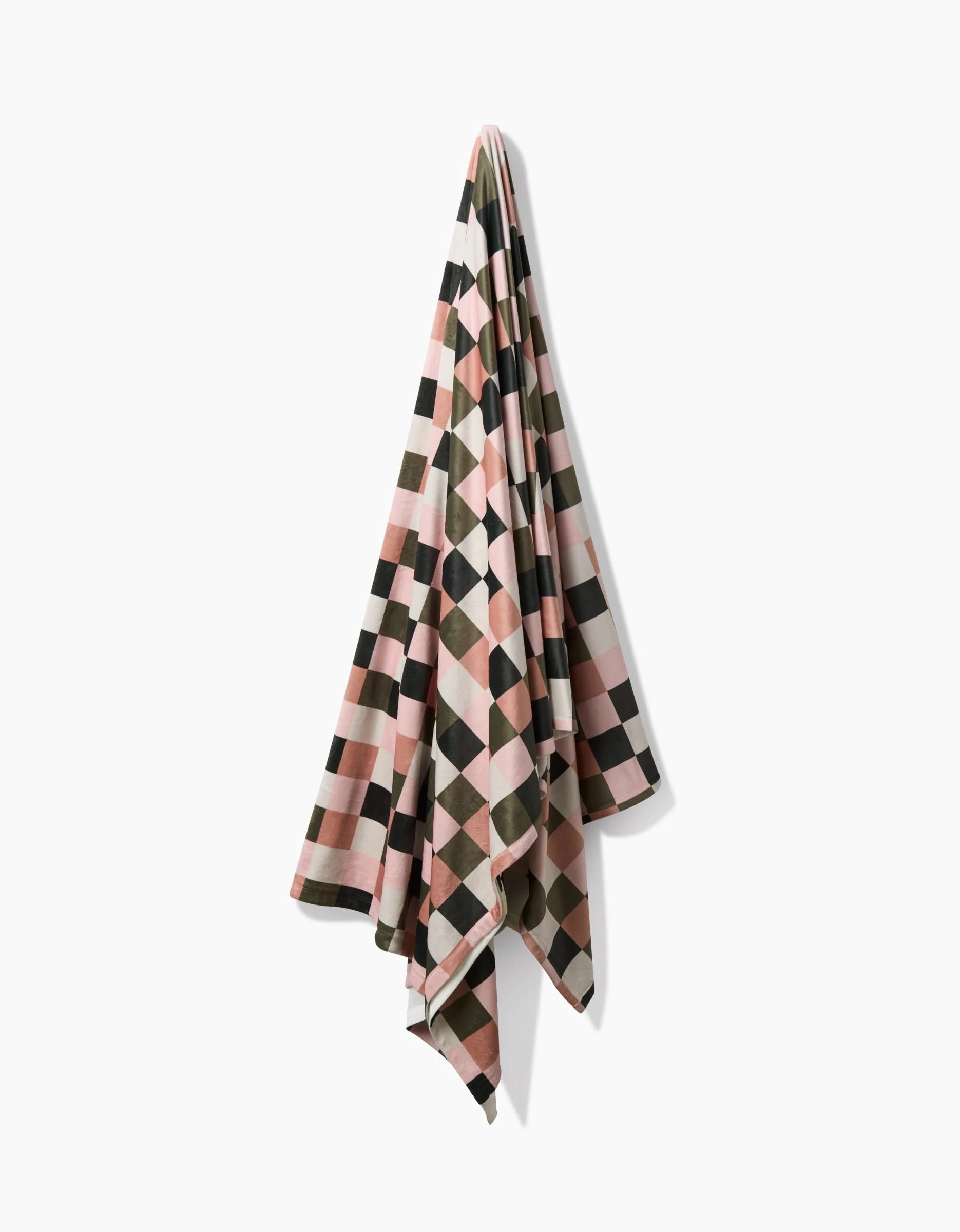 A Luxora Butter Blanket by Geometry, featuring pink, black, white, and olive green squares in a geometric pattern, is draped against a plain white background—crafted from recycled materials for sustainability.
