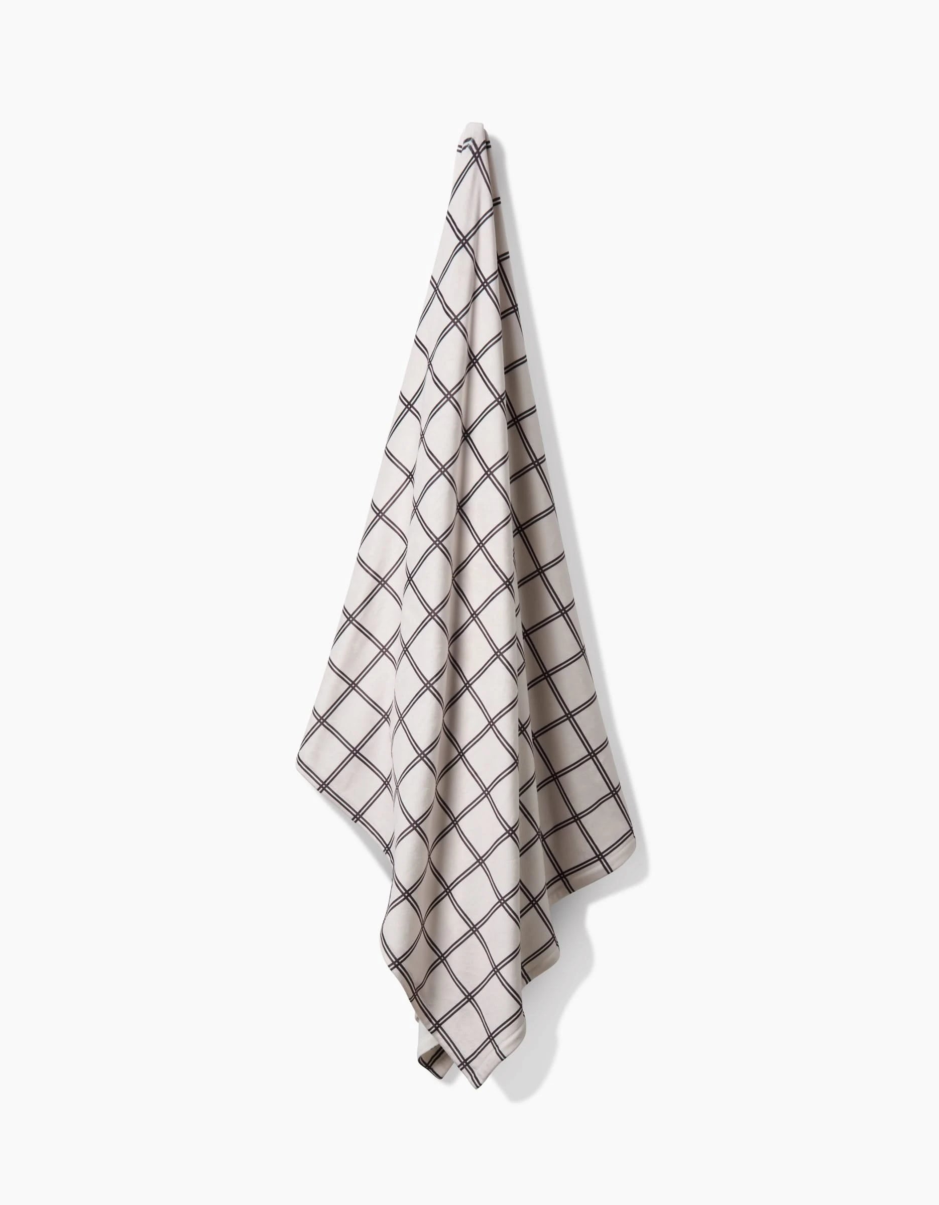 The Geometry Moon dish towel, featuring a black grid pattern on white and made from recycled materials, hangs against a white background.