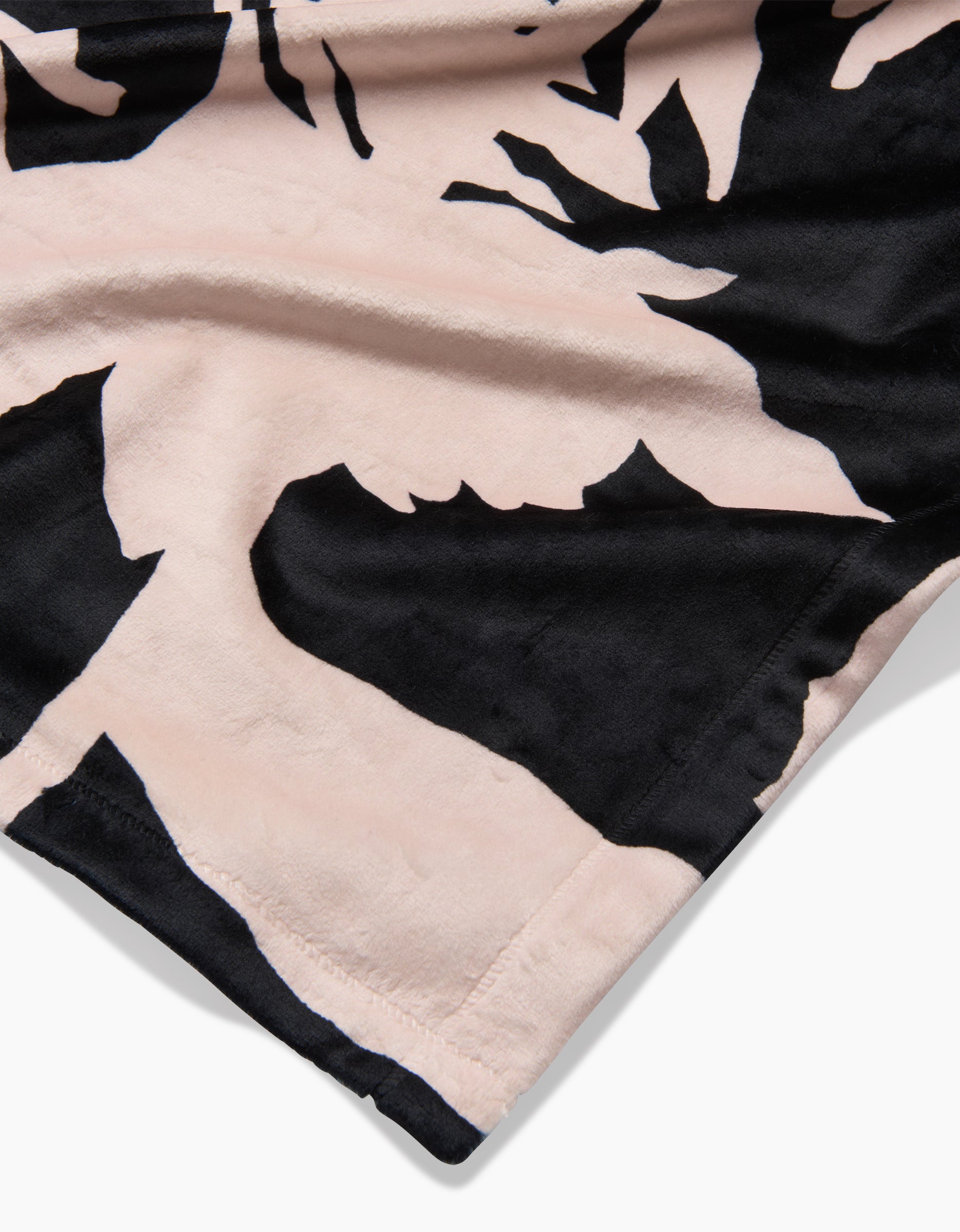 Close-up of Geometrys Pam fabric, showcasing a black and light pink abstract pattern on recycled material, with detailed edge stitching and a velvety, silky-soft texture.