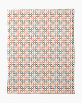 The Russet Crossroads Butter Blanket by Charlie Rowan Designs features a symmetrical geometric pattern of black squares and orange lines on white, crafted from recycled materials for an eco-friendly, stylish look.