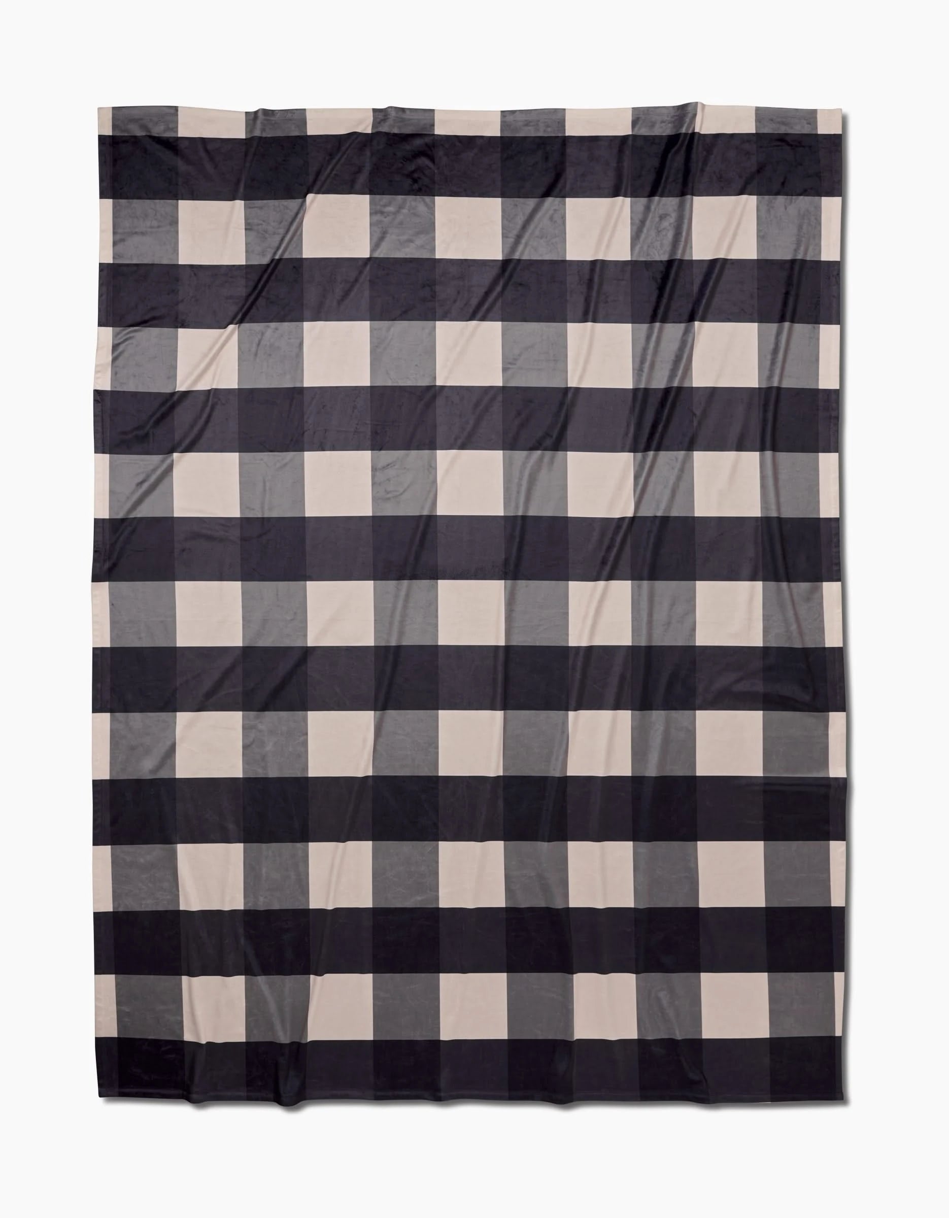The Snowy Gingham Butter Blanket by Geometry features a large black and beige checkered pattern, laid flat on a white background. Made from recycled materials, the fabric shows visible folds and creases.
